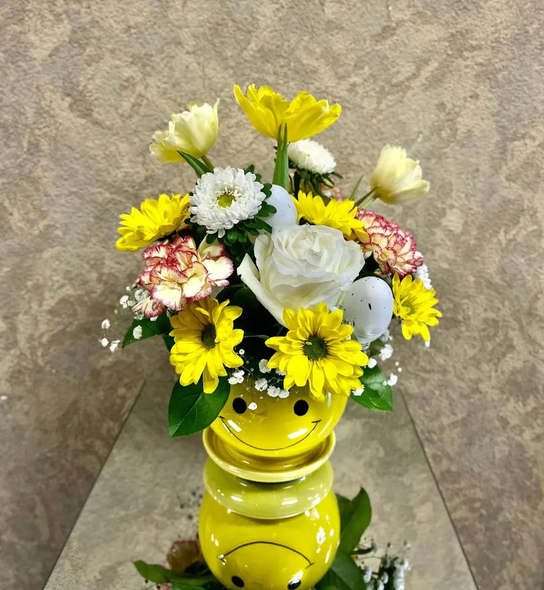 Yellow and white flower arrangement in a smiley-face vase