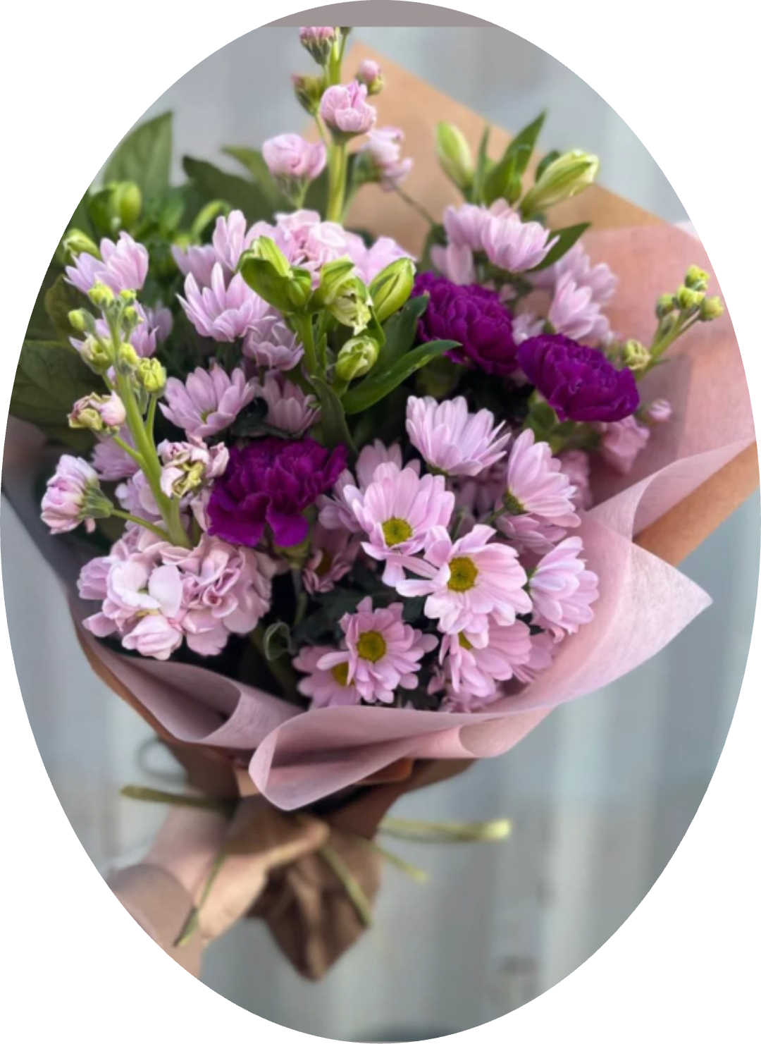 PURPLE DAISY BOUQUET - Soft pink daisies and pale pink carnations meet pops of vivid purple in a cheerful hand-tied flower arrangement perfect for birthdays, spring celebrations, or a just-because surprise. This bouquet reads feminine and fresh-the layered contrast between pastel blooms and saturated purple accents creates an immediate, uplifting impression that will make the person you're thinking of feel seen and celebrated.  The mix includes daisy-like chrysanthemums, alstroemeria, carnations, and chrysanthemums in stages from tight buds to open blooms, so the texture feels full and naturally lively. Wrapped in blush and brown paper with a neat ribbon, the presentation keeps a lightly romantic, artisanal look-easy to carry and display in a casual vase. Colors are pink, purple, white, and green, giving a versatile palette that complements many home décors.  Ideal for everyday gifting, Mother's Day, or sending cheerful wishes, this bouquet arrives ready to brighten a room and soften a moment. Because blooms arrive at varying stages, they'll continue to open over several days; trim stems and change the water regularly to extend their freshness.