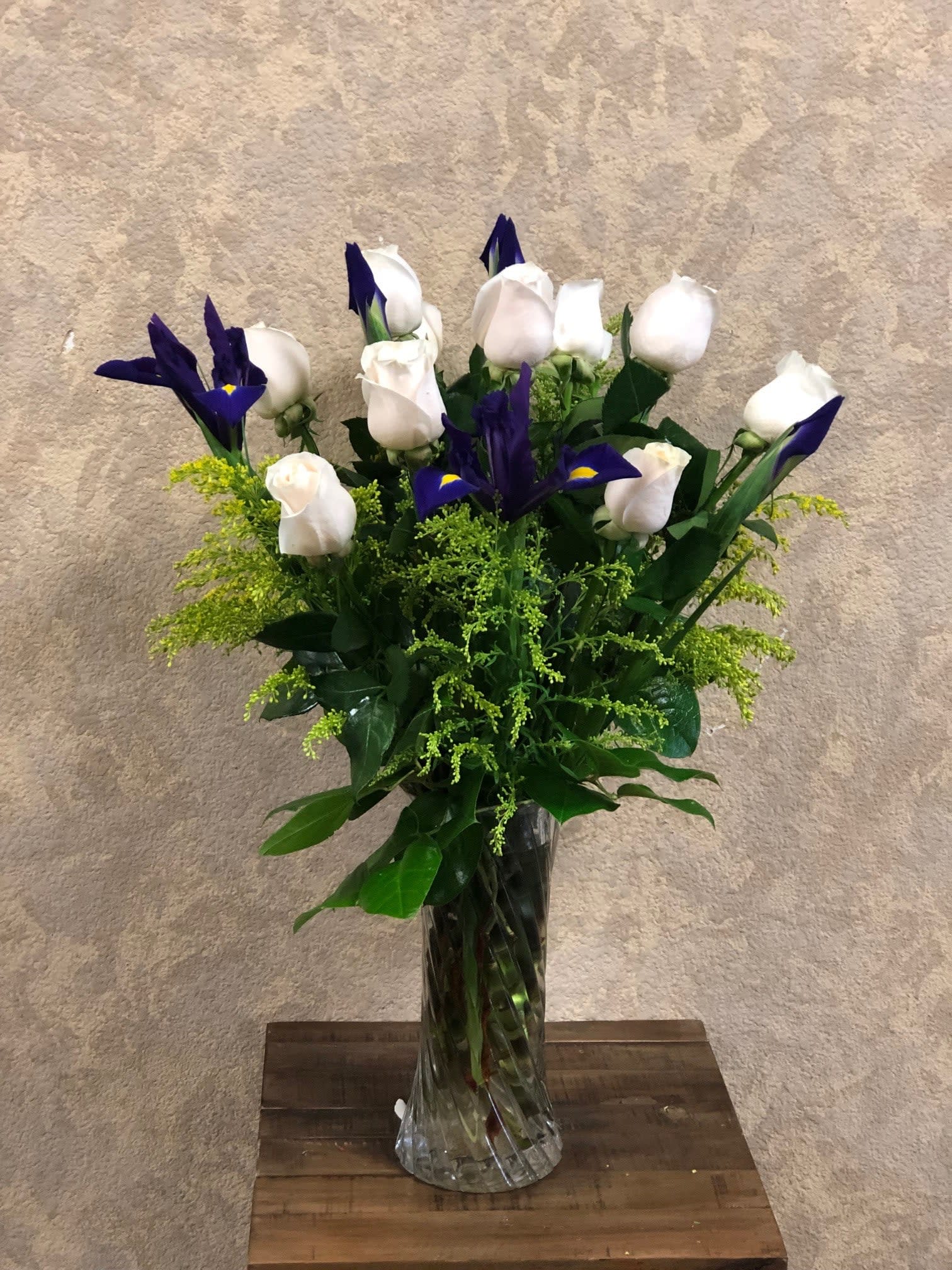 Marbella - Type of Flowers: White Roses and Blue Iris in a tall medium vase. Availability: All year round Substitute Available: Yes Design View: All-sided Facing View Photo shown: Regular
