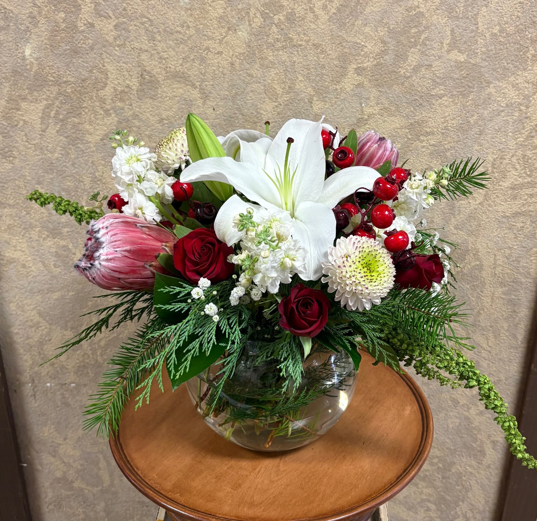 Sophisticated Winter Birthday - Holiday accents can be added. Please see second picture  Recipe: White Lilies, White Stock, Protea, White Mums, Red Roses, Green Amaranthus, Pine branches, Red Berries in a bumble bowl vase. Seasonal: All year round Orientation: All Facing View Photo shown: Standard 
