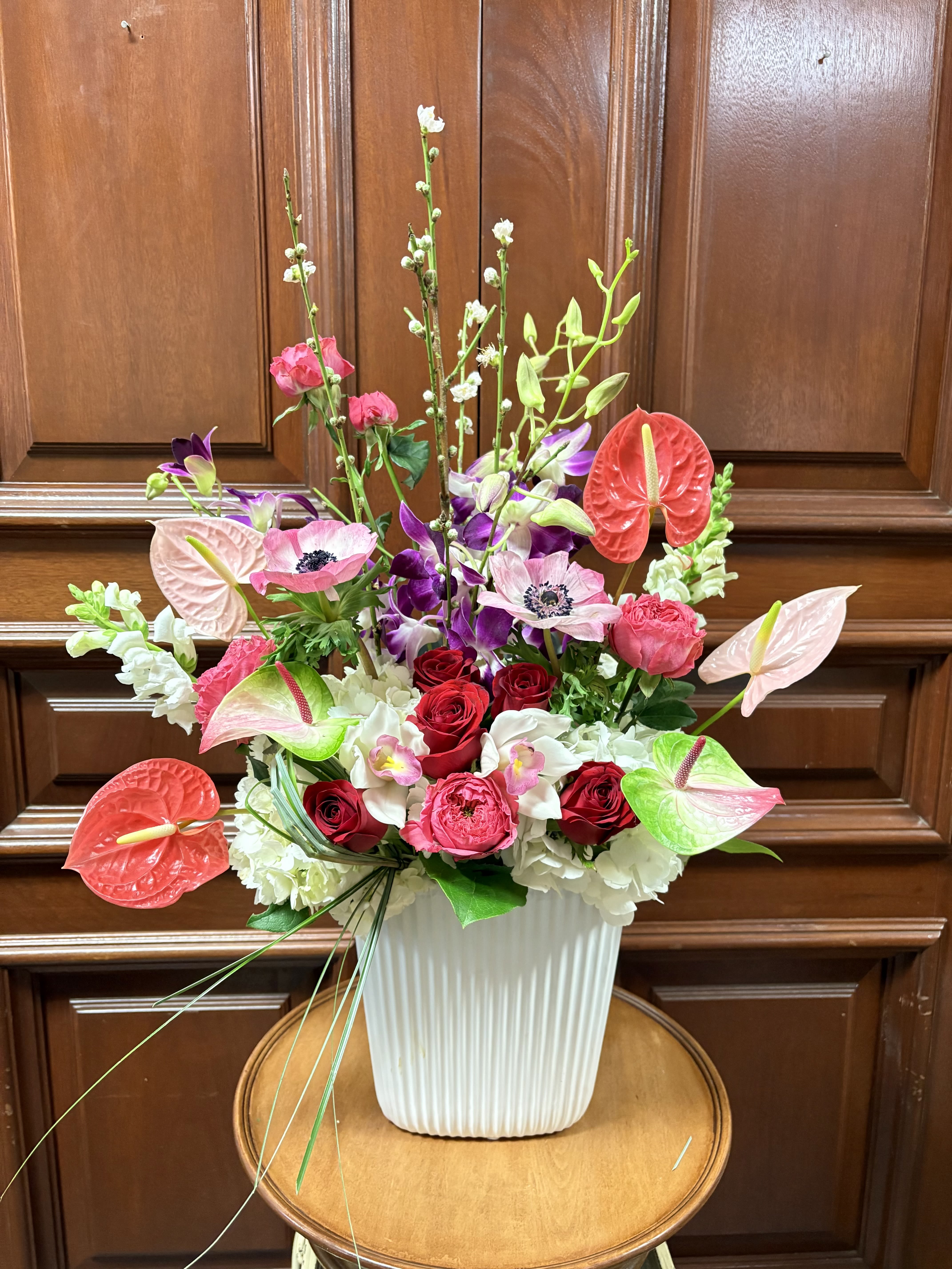 Hello Gorgeous! - Recipe: Seasonal Pink Anemones, Seasonal Cherry Blossoms, Anthurium, White Hydrangaes, Purple Dendrobium Orchids, White Cymbidium Orchids, White Snapdragons, Red Roses, and Pink Garden Roses in a tall, white vase. Seasonal: Seasonal Orientation: Front Facing View Photo shown: Standard