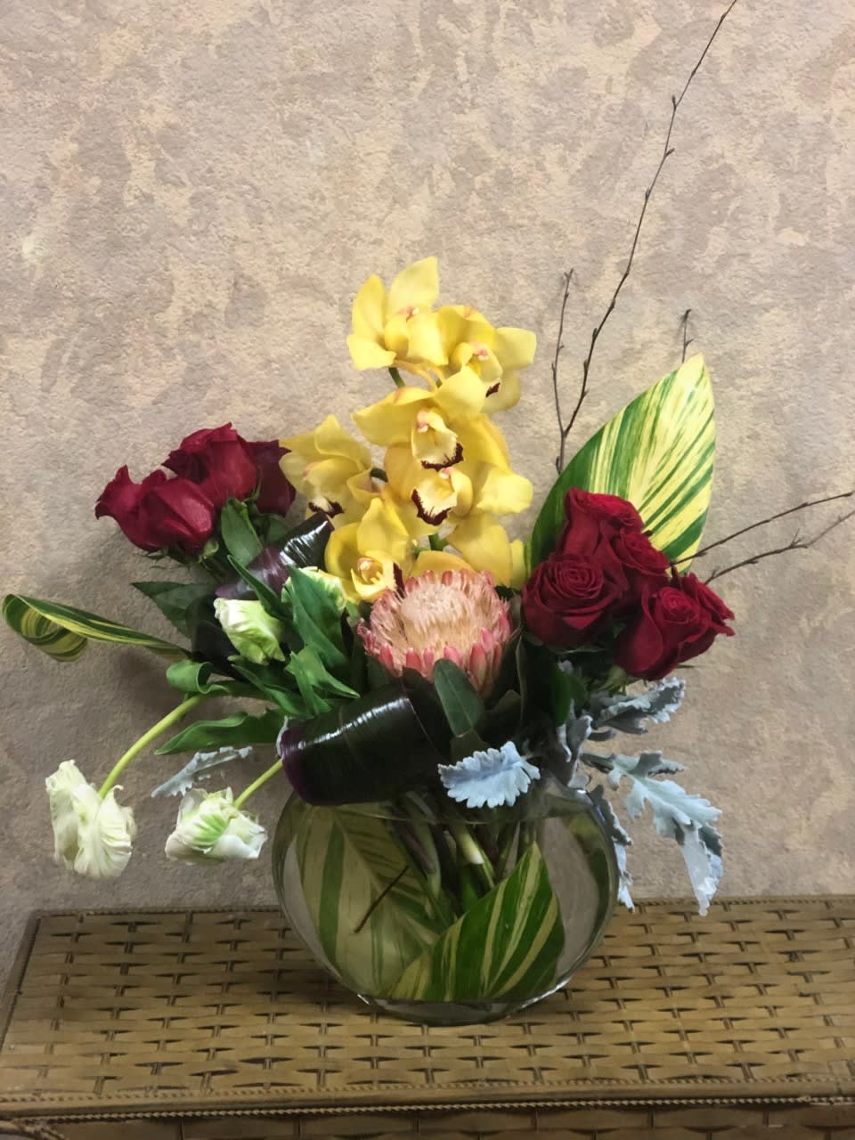 Enchanted Lady - Type of Flowers: Yellow Cymbidium Orchids, King Protea, Red Roses, White Parrot Tulips, Dusty Miller, Birch Willow Branches, and Leaves in a short vase. Availability: All year round Substitute Available: Yes Design View: All Facing View Photo shown: Regular 