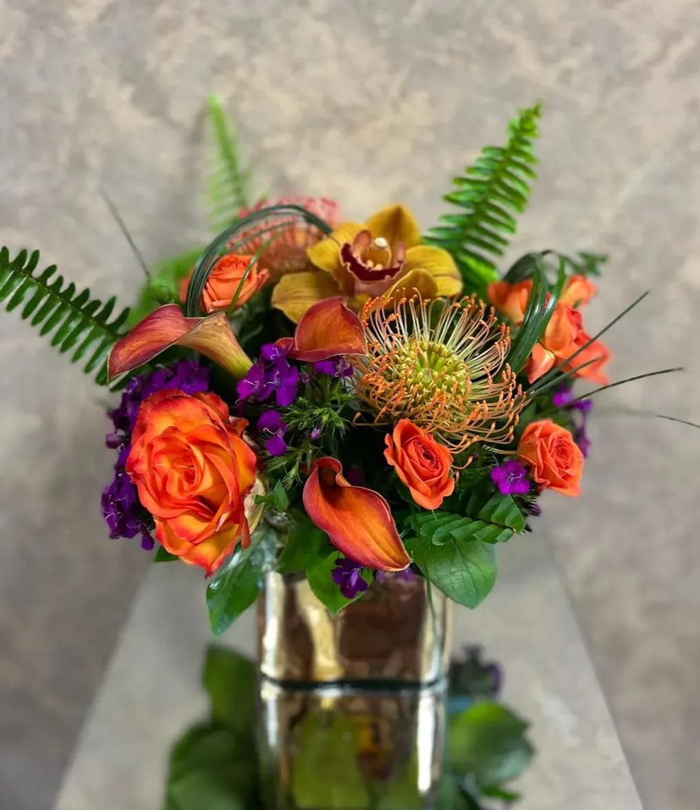 Marble Canyon, Arizona - Recipe: Cymbidium Orchid, Orange Protea, Orange tipped Roses, Calla Lilies, Sweet Williams, Spray Spray Roses in a short, gold vase. Availability: All year round Substitute Available: Yes Design View: Symmetric Front Facing View Photo shown: Regular 