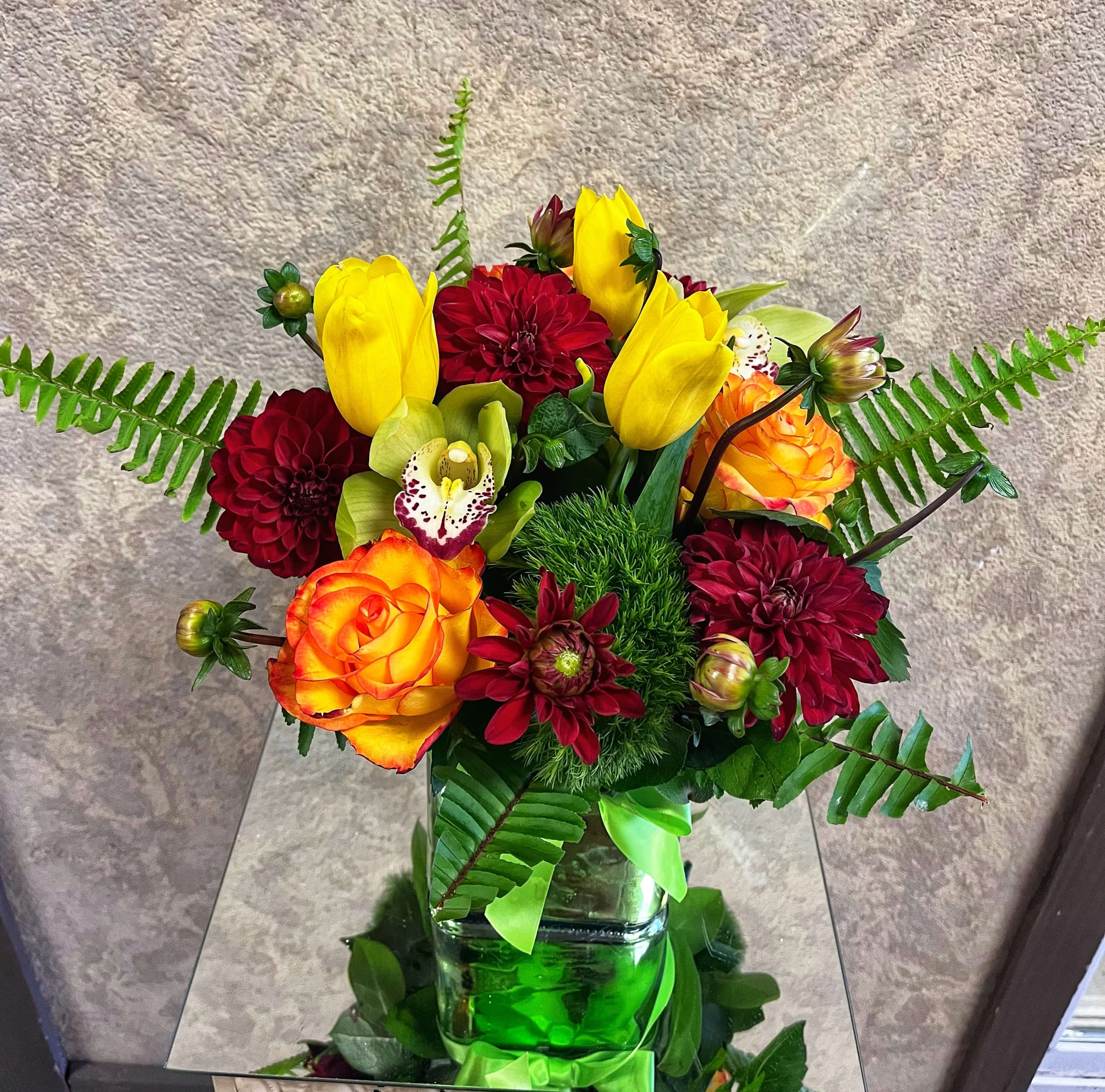 Mango Tango - Get a summery tang with a mix of nature's green Cymbidium Orchids, Fiery-red Dahlias, Bright Yellow Tulips and Hybrid Orange Roses in a green vase with ribbon. Availability: All year round Design View: Symmetric Front Facing View Photo shown: Regular