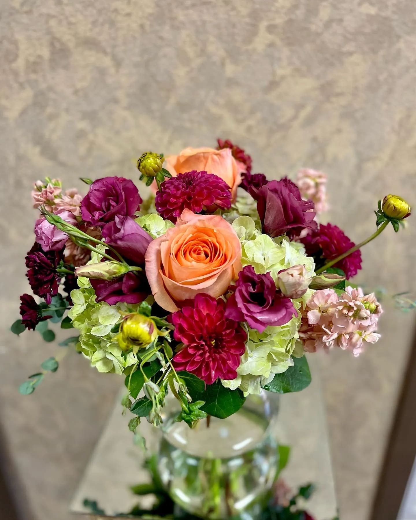 Mariposa - This arrangement includes Seasonal Pink Dahlias, Beautiful Magenta Lisianthus, Green Hydrangeas, Pale Pink Stock, and Orange Roses in a circular, crystal vase. Availability: All year round Design View: Symmetric Front Facing View Photo shown: Regular 