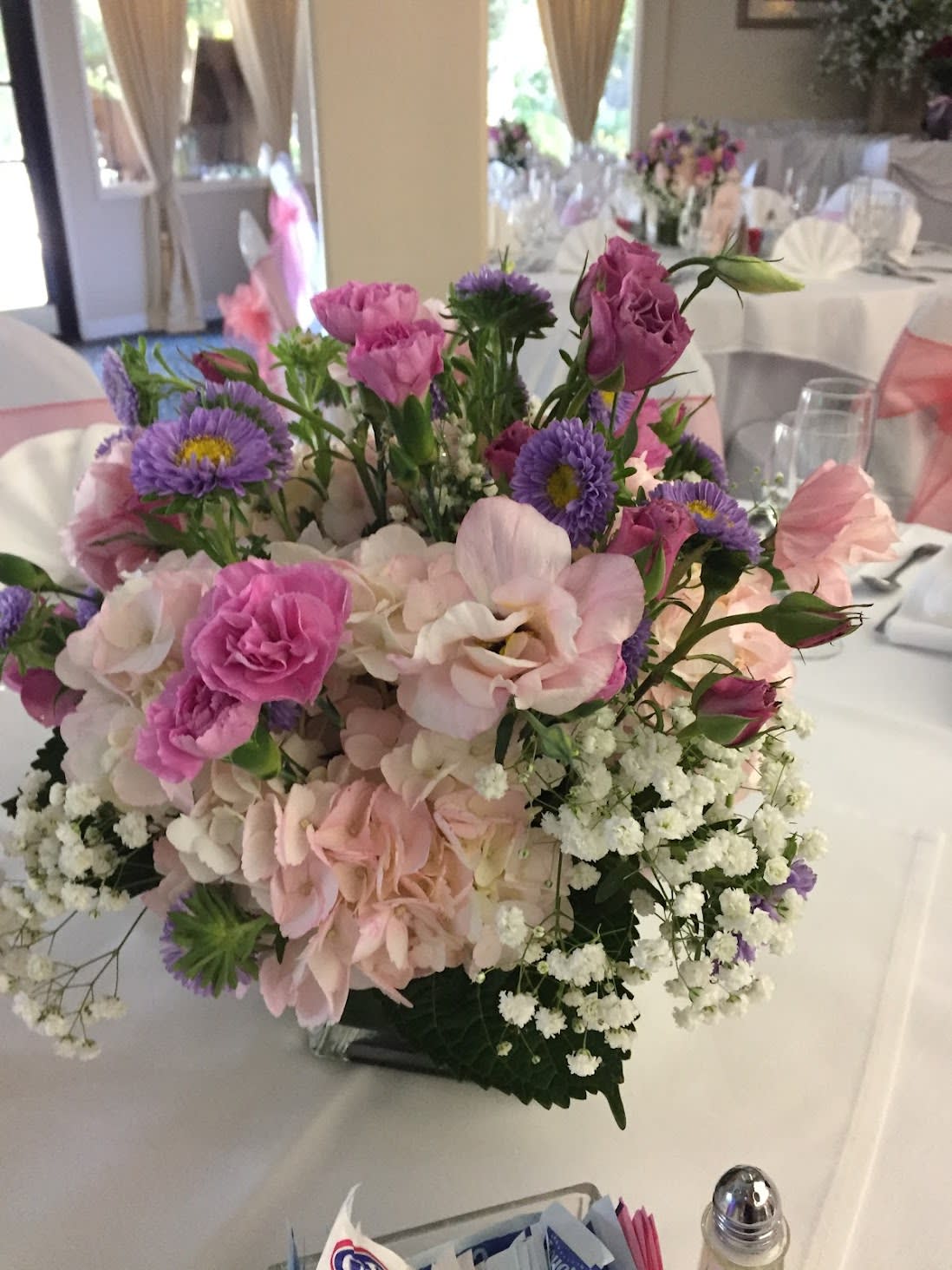 Sweet Pea Centerpiece - Sweet Pea centerpiece has Magenta and Pink Lisianthus, Purple Matsumoto Asters, Pink Hydrangeas, and Babies Breath in a clear cube vase.