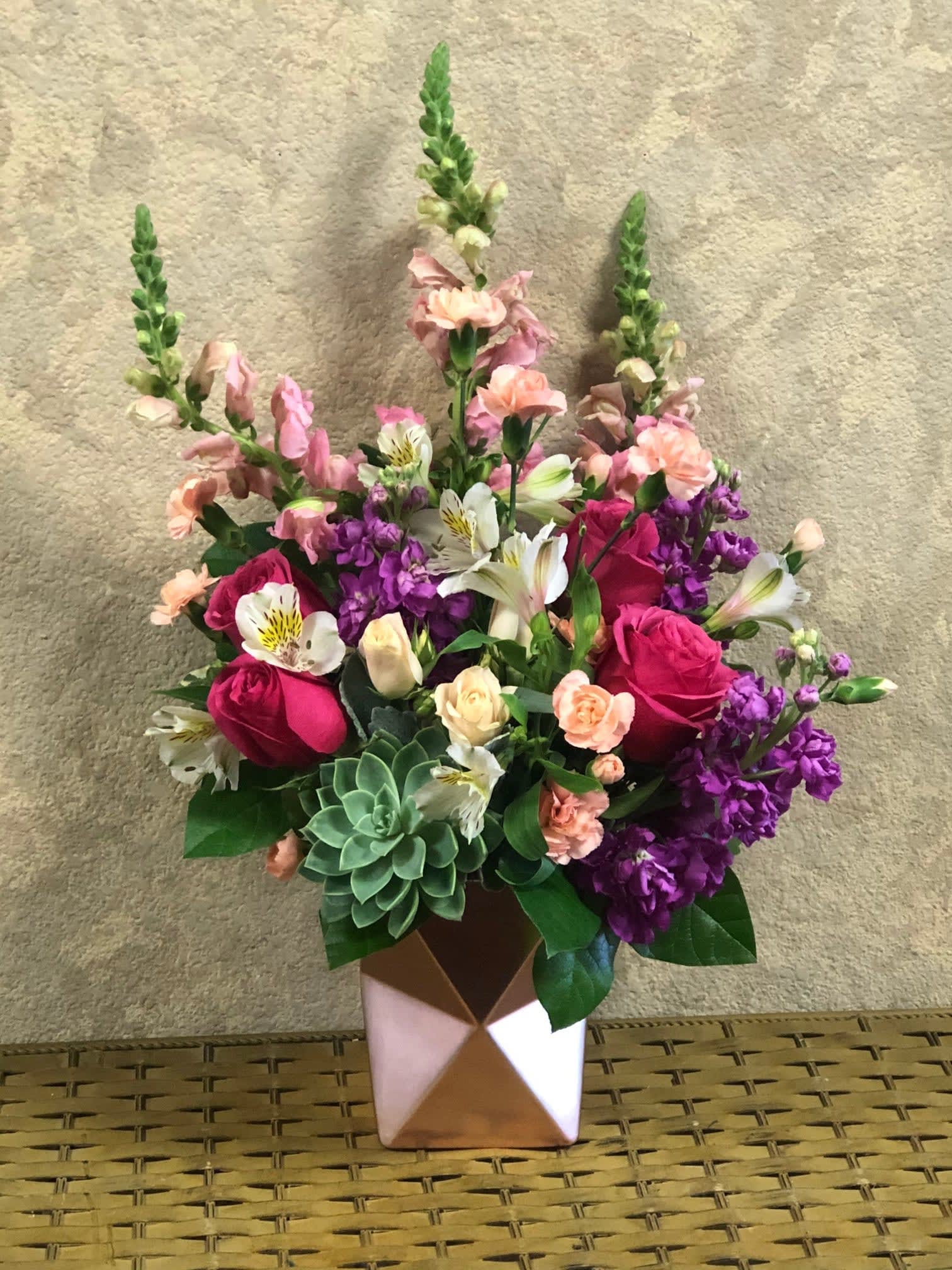 Magnificent Pink Prism - Type of Flowers: Pink Snapdragons, Purple Stock, White Spray Roses, Hot Pink Roses, Mini Pink Carnations, White Alstroemerias, and green Succulent in a rose pink vase. Availability: All year round Substitute Available: Yes Design View: All Facing View Photo shown: Regular