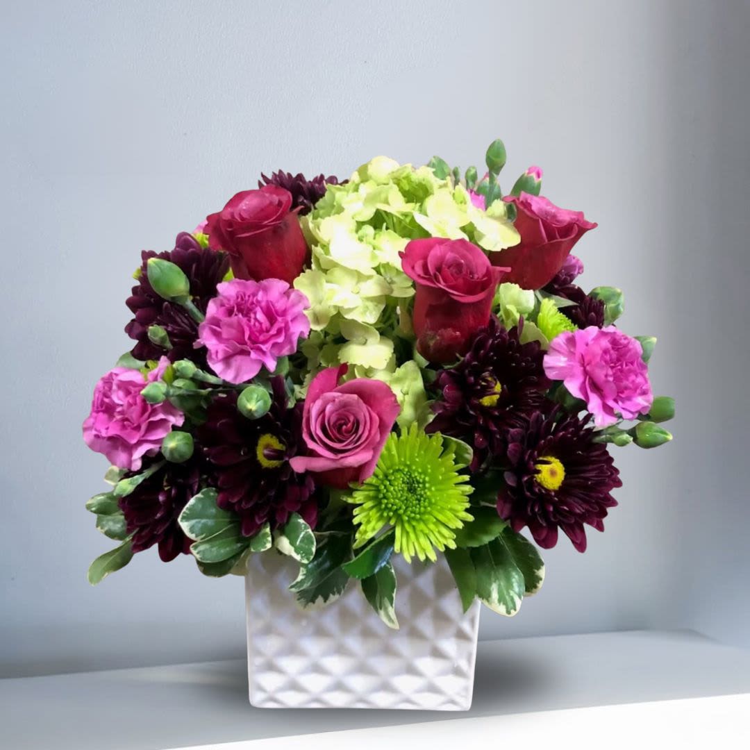 Congratulations Grad - Type of Flowers: Lavender Roses, Green Hydrangeas, Purple Daisies, Green Button Mums, Lavender Carnations, and greens in a square ceramic vase. Availability: All year round Design View: Symmetric Front Facing View Photo shown: Regular