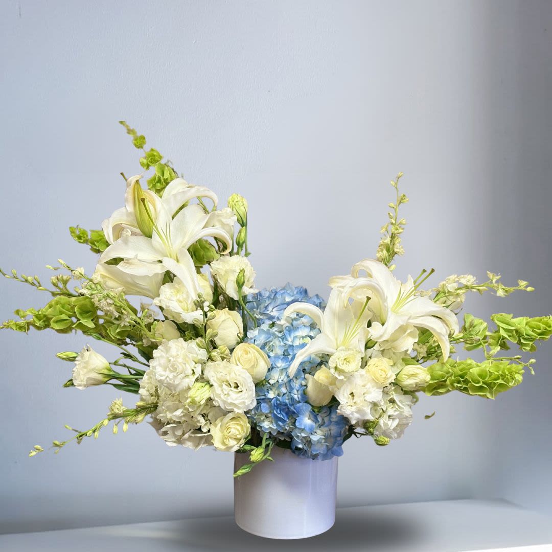 Sea of Love - Send your love and healing thoughts with this elegant sympathy piece.  Recipe: White Casablanca Lilies, White Lisianthus, Blue and White Hydrangeas, White Roses, White Dendrobium Orchids, Bells of Ireland in a white, circular vase. Seasonal: All year round Orientation: Front-Facing View Photo shown: Standard