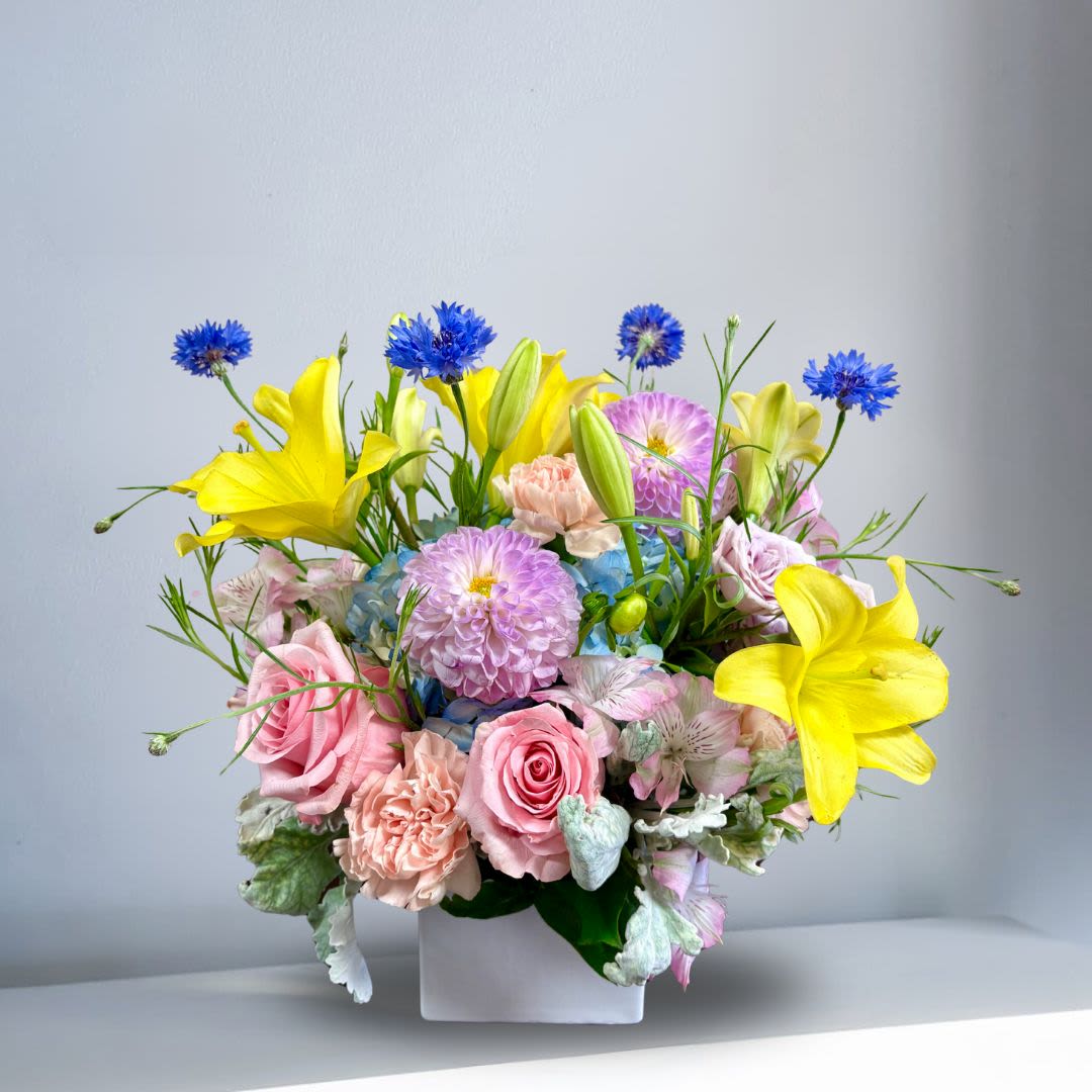 Inner Light - Recipe: Yellow Lilies, Seasonal Dahlias, Alstromerias, Spray Roses, Hydrangeas and more in a square, white vase. Seasonal: Seasonal Dahlias Orientation: Front-Facing View Photo shown: Standard 