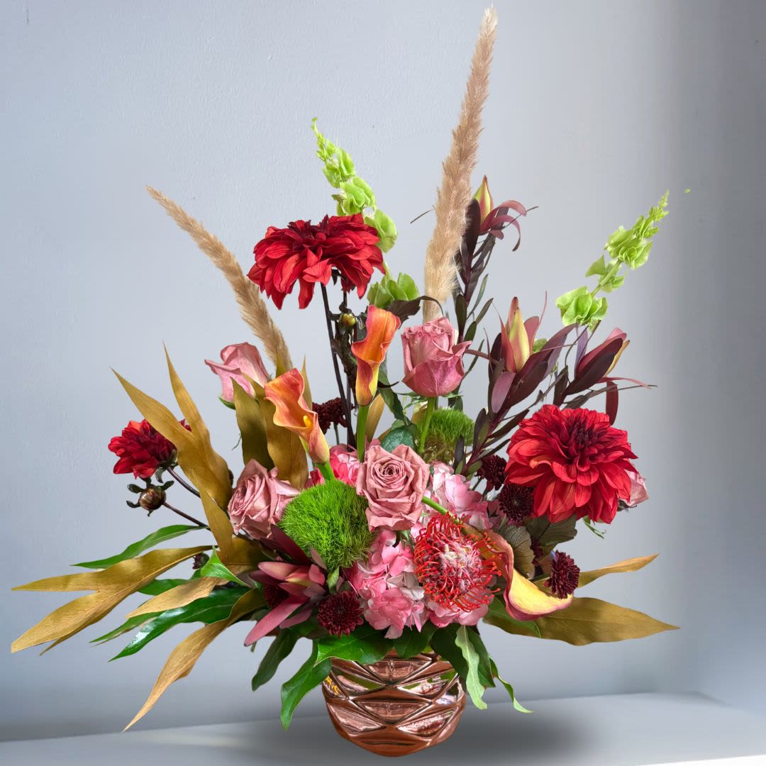 Efflorescent - Recipe: Seasonal Red Dahlias, Calla Lilies, Hydrangeas, Mauve Roses, Protea, Bells of Ireland, Cone Brush Safari, Dianthus, and more in a rose gold vase. Seasonal: Seasonal Dahlias Orientation: Front Facing View Photo shown: Standard 
