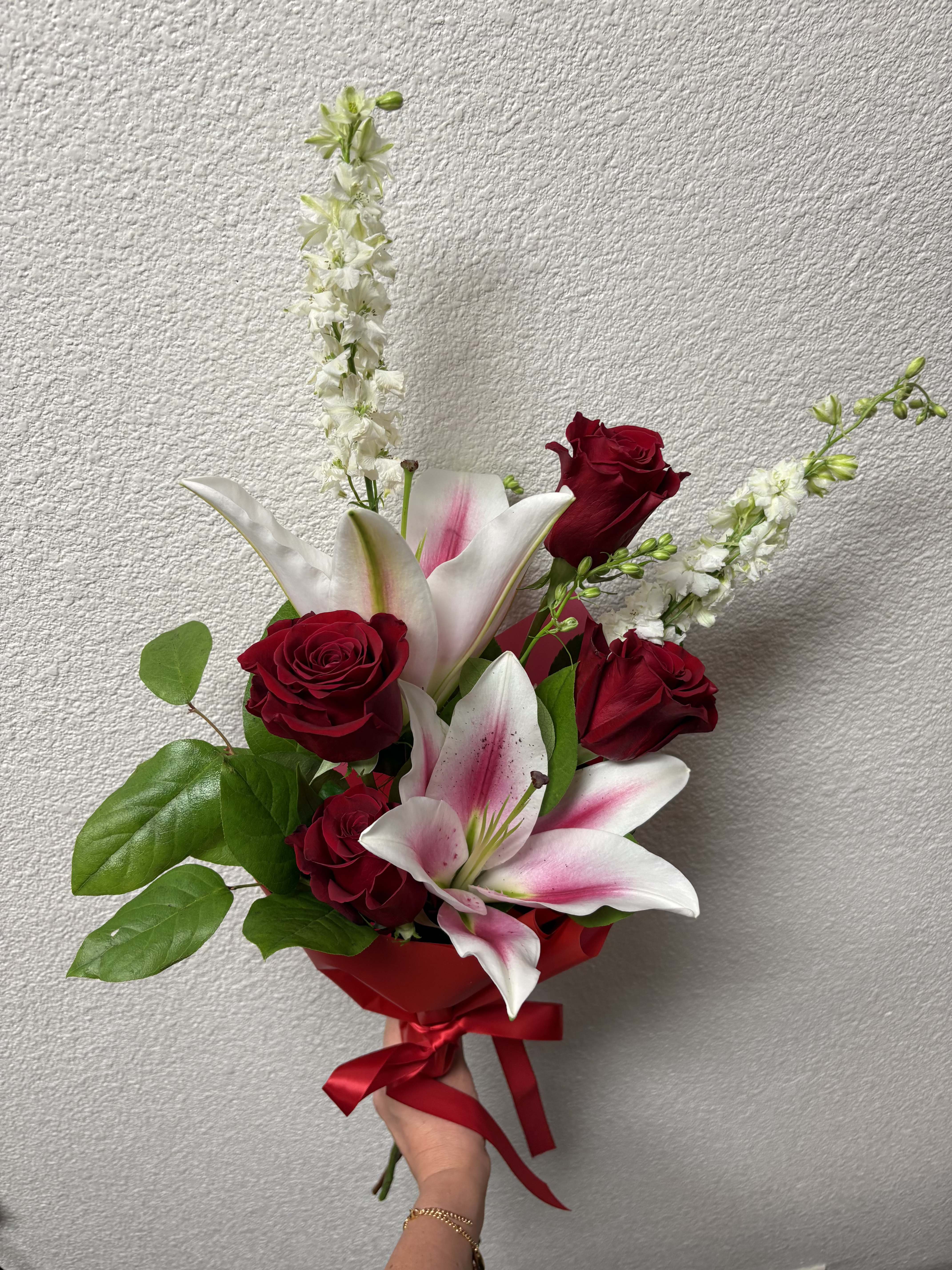 Hand-tied bouquet of red roses and pink lilies with a red ribbon