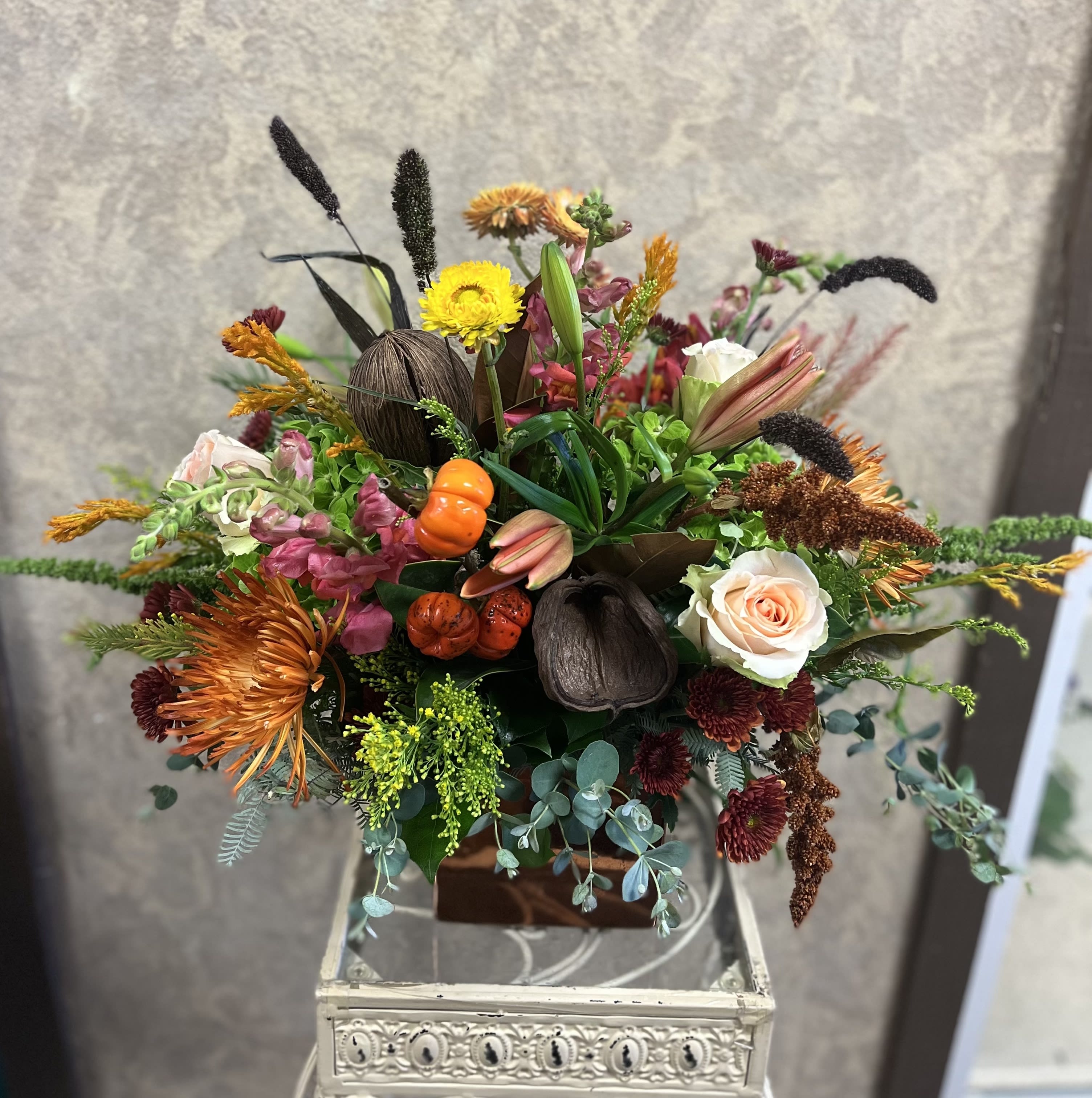 The Wild, Come Together Centerpiece - This Thanksgiving, gather around this wildly vibrant, fall centerpiece that includes fresh Snapdragon, Peach Roses, Pink Lilies, Wheat, Sterculia Pods, Chrysanthemums, Amaranthus, and more in a brown vase. Availability: All year round Design View: All Facing View Photo shown: Regular 