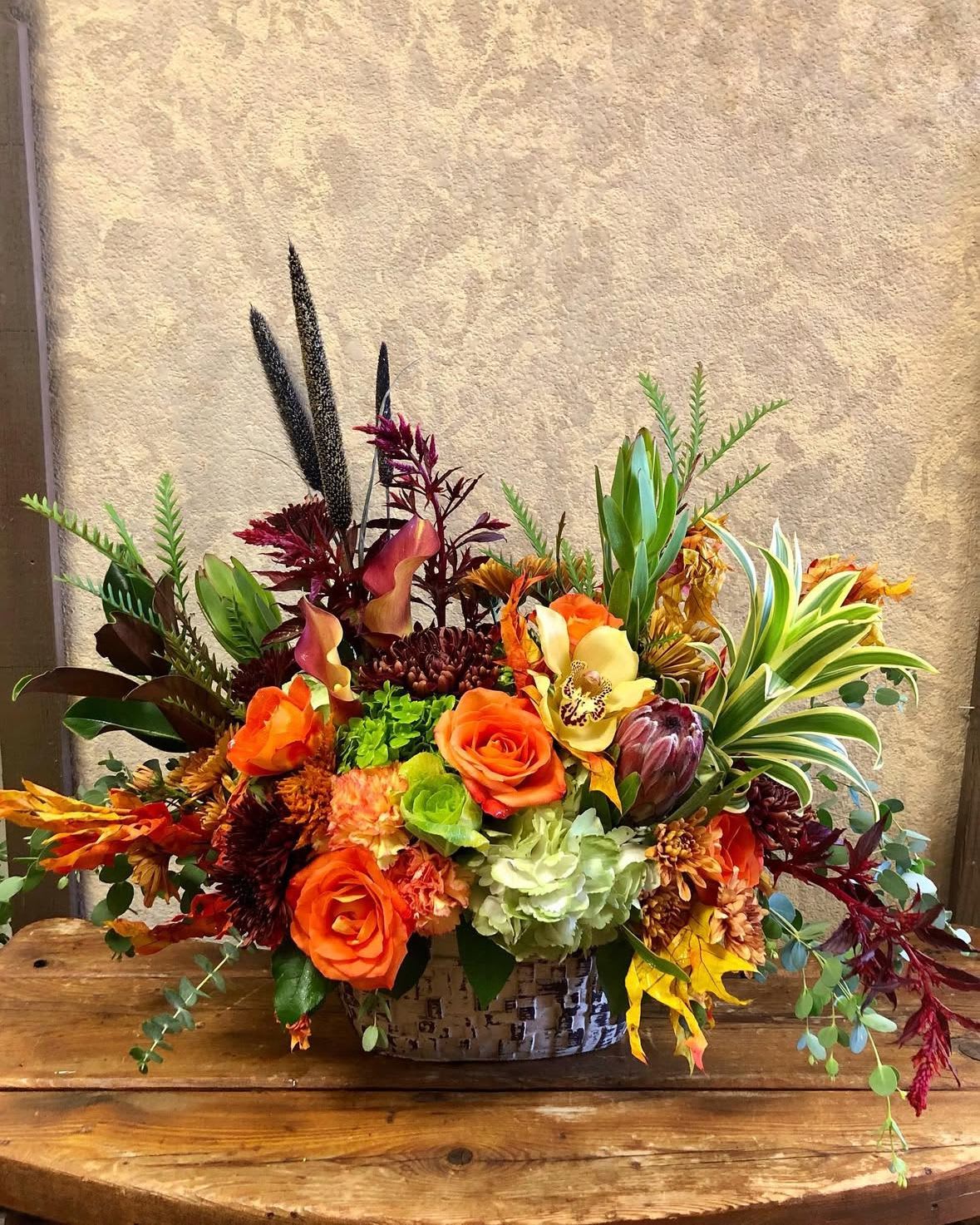 Free fallin - This is a great Friendsgiving gift or family wishes this holiday season.  Type of Flowers: Purple Calla Lilies, Orange Roses, Cabbage, Hydrangea. Spider Mums, Amaranthus, Protea Cymbidium Orchids, Carnations, and more in a bark wood like vase.  Availability: Fall Orientation: Symmetric Front Facing View Photo shown: Standard
