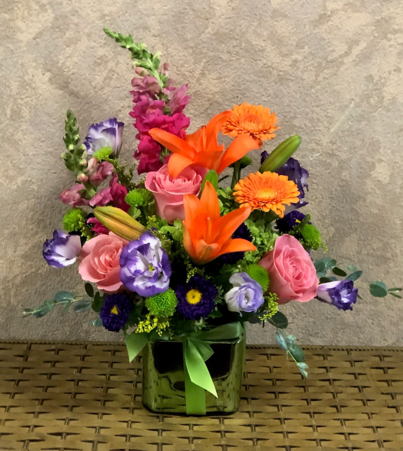 You've Got A Friend in Me - This popular, colorful arrangement is great to celebrate friendship, birthdays, or just because.  Recipe: Purple Snapdragon Orange Gerberas, Pink Roses, Orange Asiatic Lilies, Purple Lisianthus, Green Hydrangae, and more in a green square vase 6" wrapped in green ribbon. Availability: All year round Substitute : Shiny green vase is no longer available, will sub for similiar. Design View: Front Facing View Photo shown: Standard