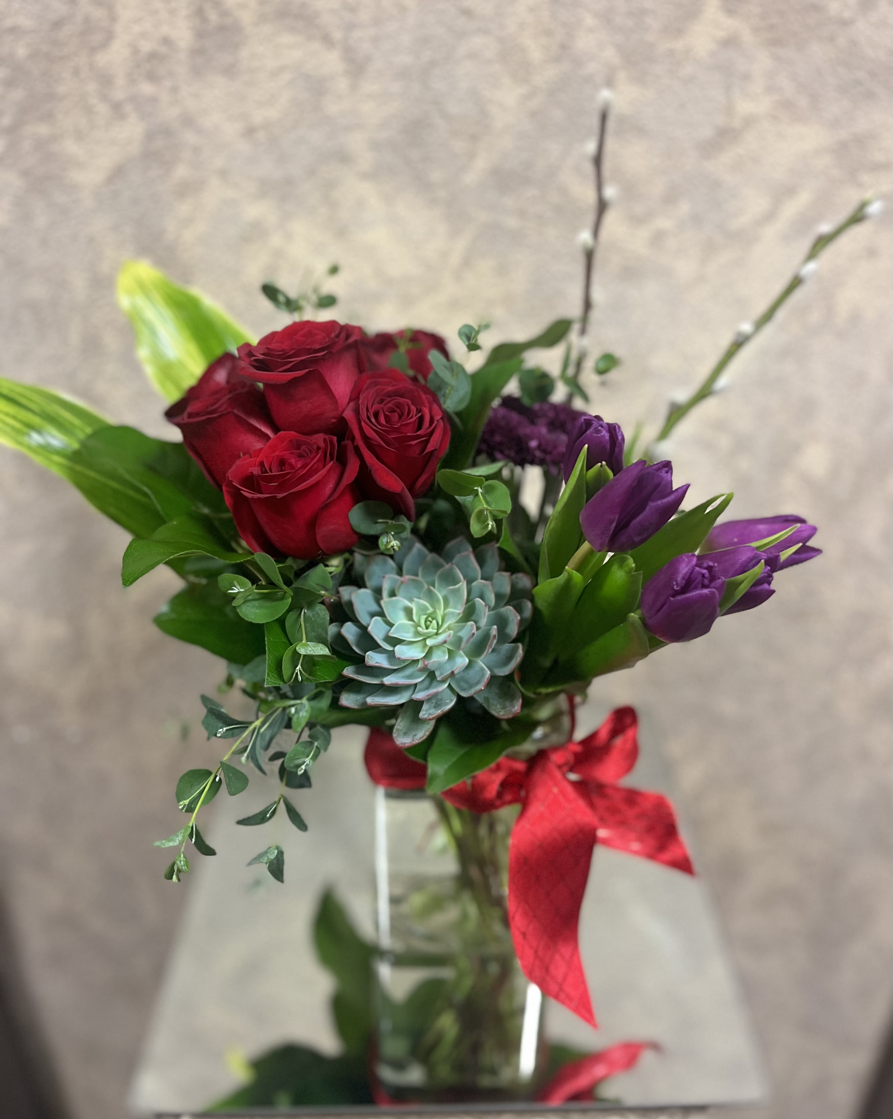 Requited Love  - Type of Flowers: Purple Tulips, Red Roses, Purple Chrysanthemums, Green Succulent, Pussy Lilies and greens in a short vase with ribbon. Availability: All year round Design View: Symmetric Front Facing View Photo shown: Standard 