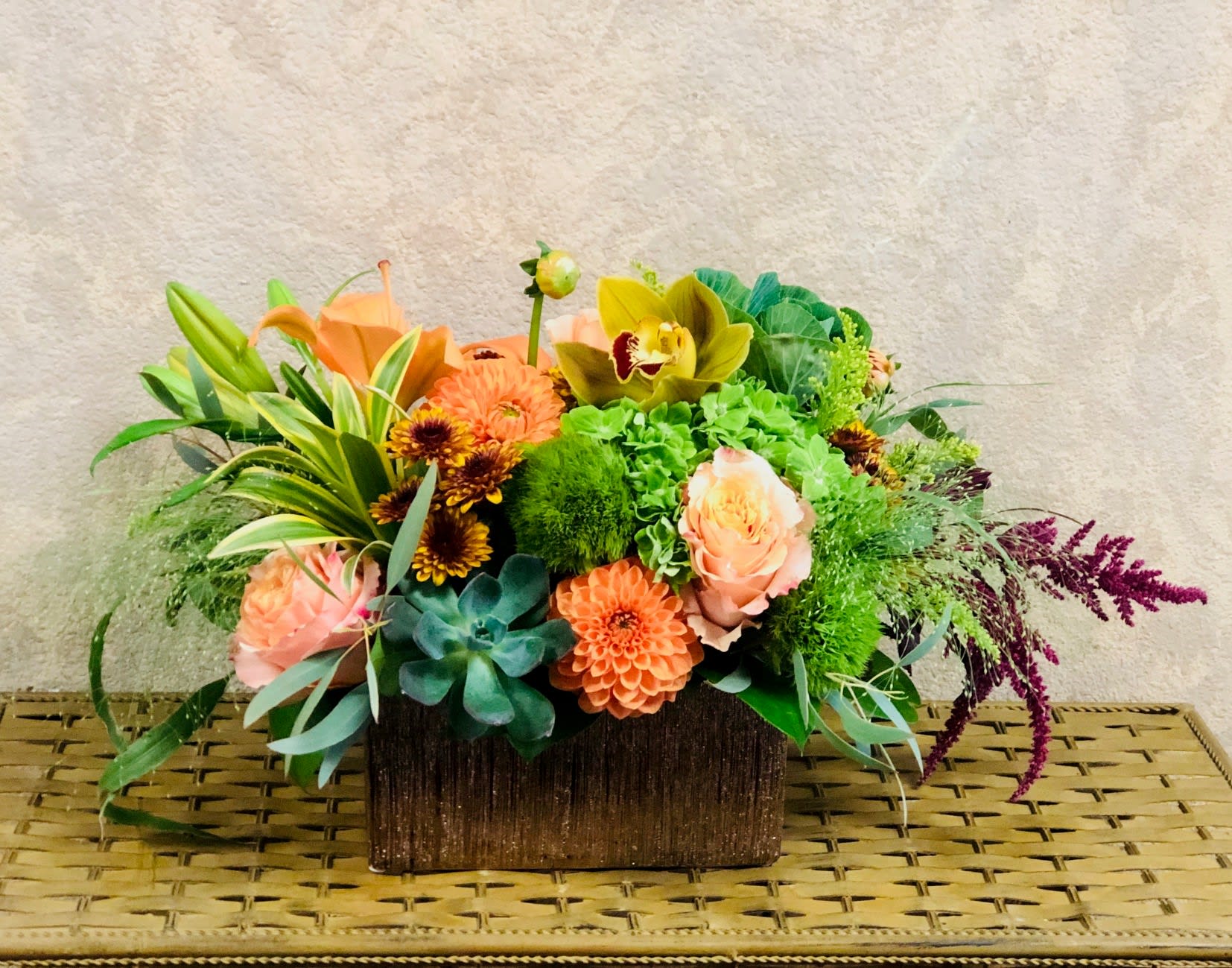 Fall Feels - Type of Flowers: Orange Dahlias, Green CYmbidium Orchids, Orange Asiatic Lilies, Pink Roses, Red Amaranthus, Fall Colored Daisies, Succulents and more in a sparkling, brown ceramic pot. Availability: All year round Substitute Available: Yes Design View: All Facing View Photo shown: Regular
