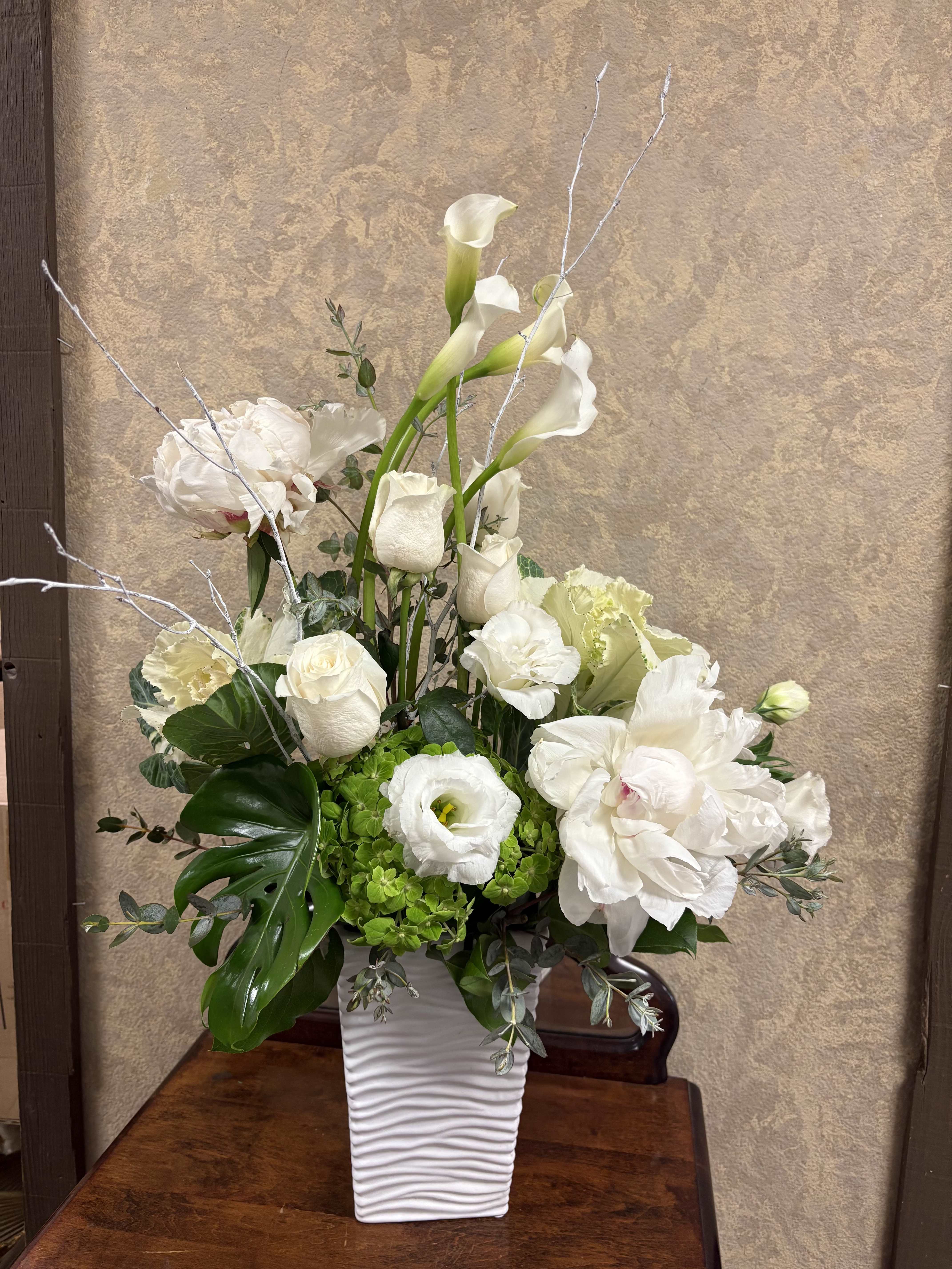 Peaceful Moments - Recipe: Seasonal Peonies, Calla Lily, Roses, Larkspur, Lisianthus, Hydrangaes, Monstera, and White Branches. Season: Seasonal Peonies Orientation: Front Facing View Picture shown: Standard Order Deluxe for Christmas