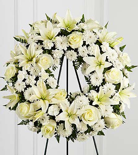 White floral wreath on a black stand with lilies and roses