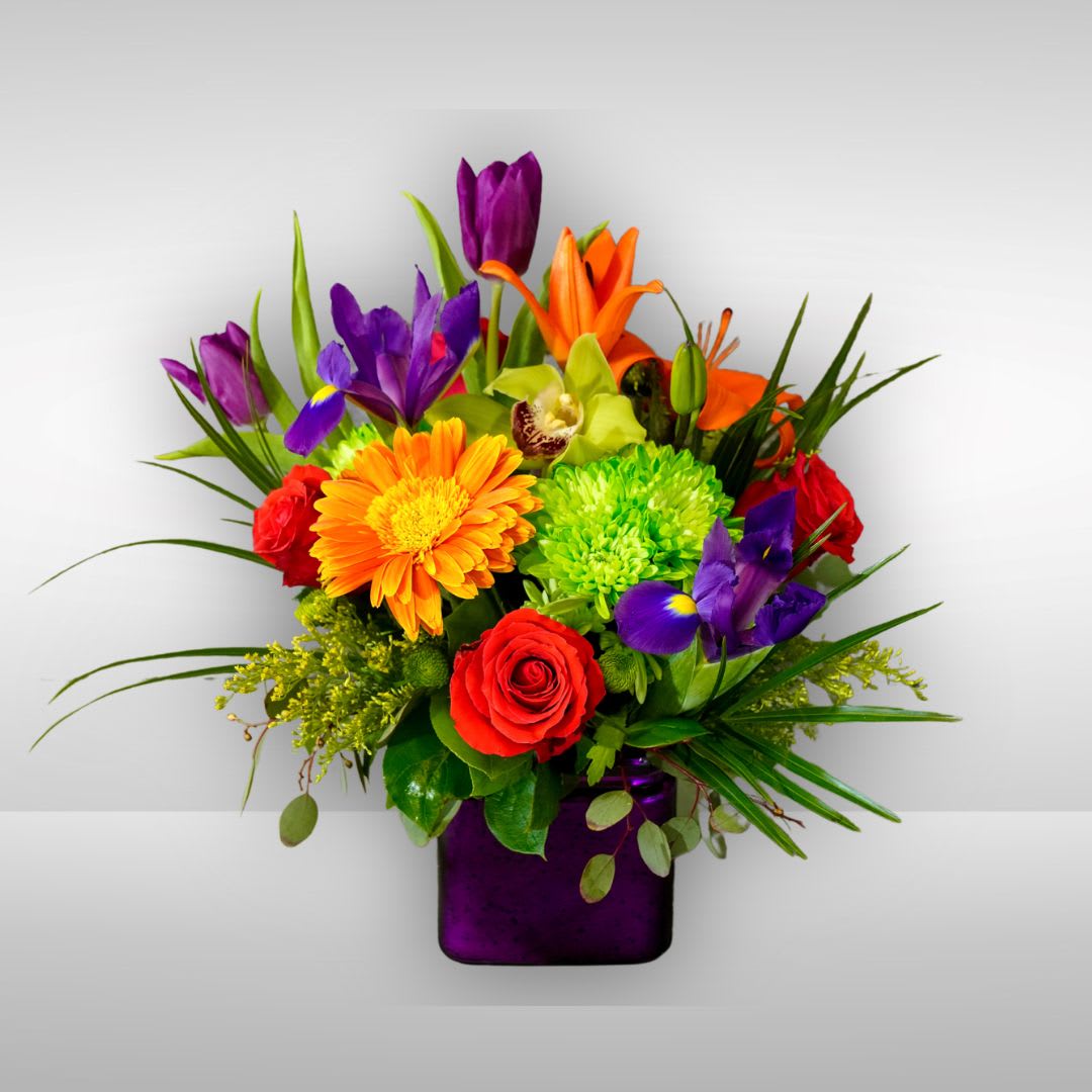 Radiate Joy - Recipe: Purple Tulips, Green Cymbidium Orchid, Orange Asiatic Lilies, Green Chrysanthemums, Orange Gerbera Daisies, Orange, Red Roses, Purple Iris and more in a short purple vase. Availability: All year round Design View: Symmetric Front Facing View Photo shown: Standard 
