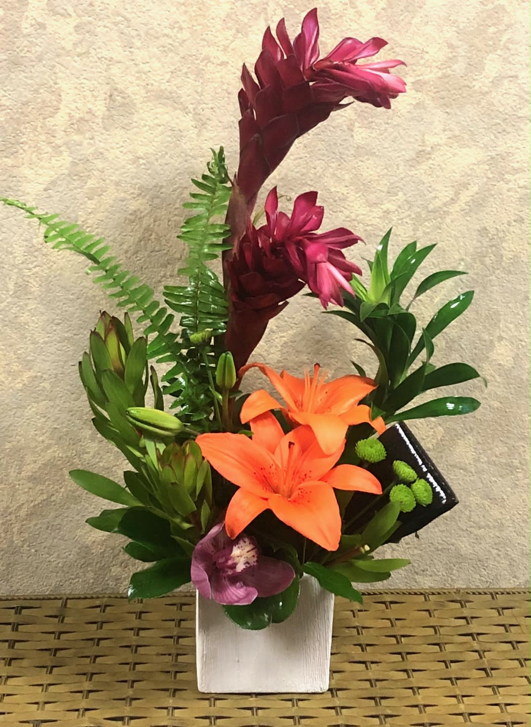 Tropical Tang - Recipe: Red Ginger, Safari, Liliies, Cymbidium Orchid and Greens in a white, cermanic square vase. Seasonal: All year round Design View: Front Facing View Photo shown: Standard 