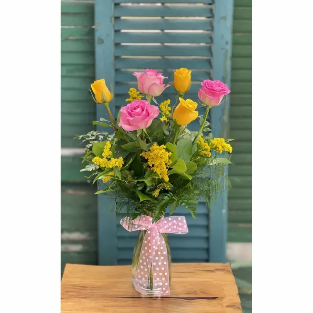 Pink and yellow roses in a clear glass vase with a pink ribbon