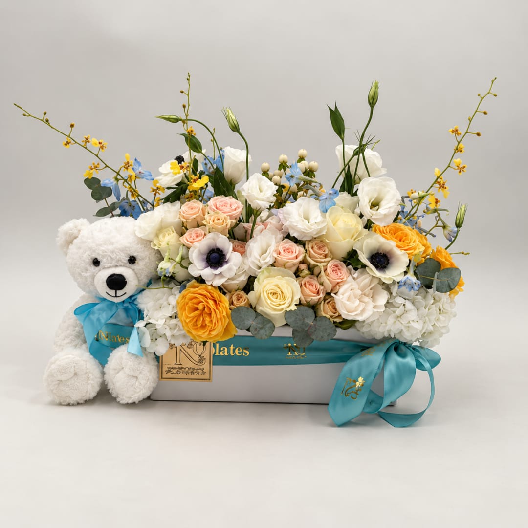 Mixed flower arrangement in a box with a teddy bear and blue ribbon