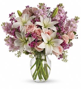 Pink roses, white lilies, and purple flowers arranged in a clear glass vase