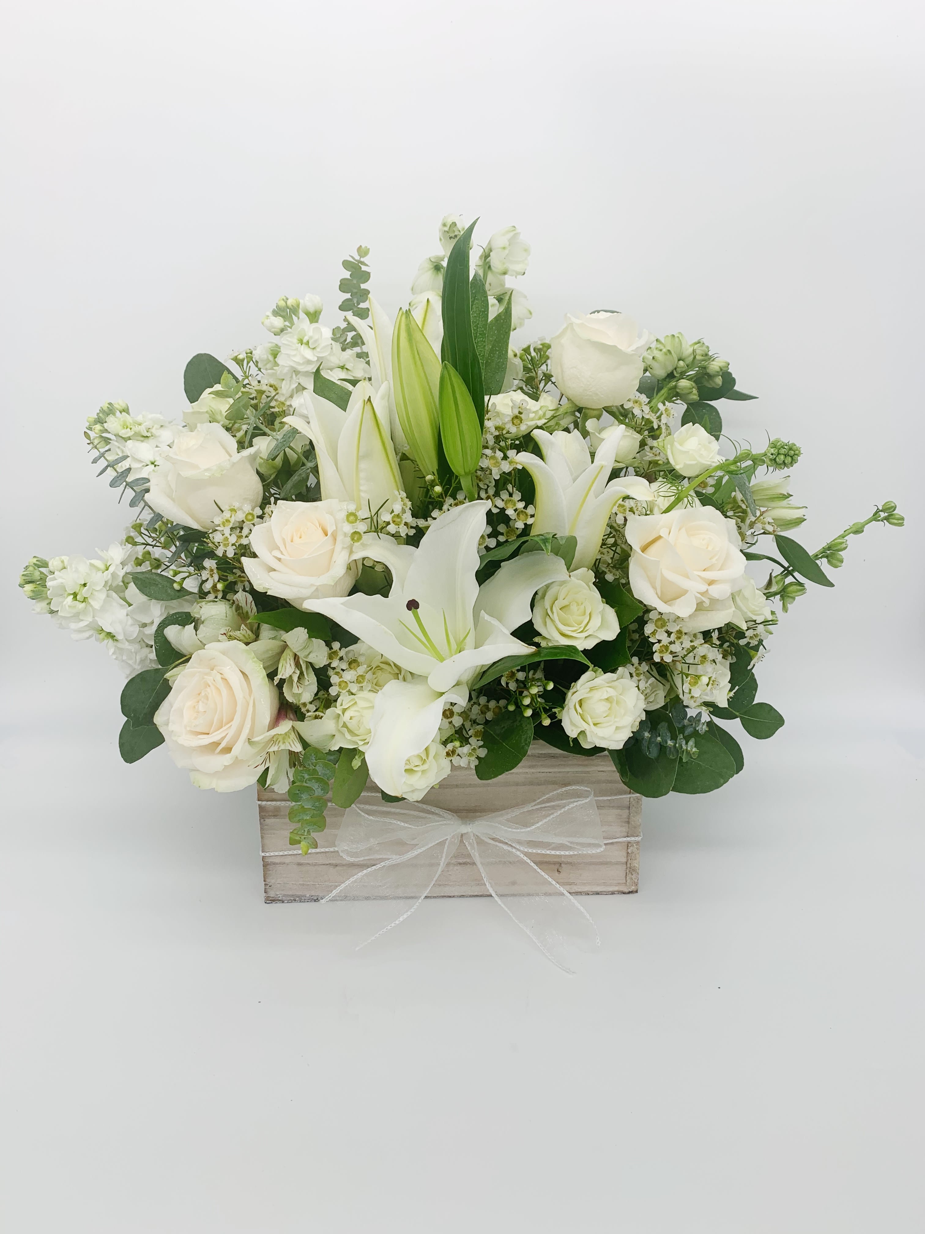 White roses and lilies arranged in a wooden box with a sheer white bow.