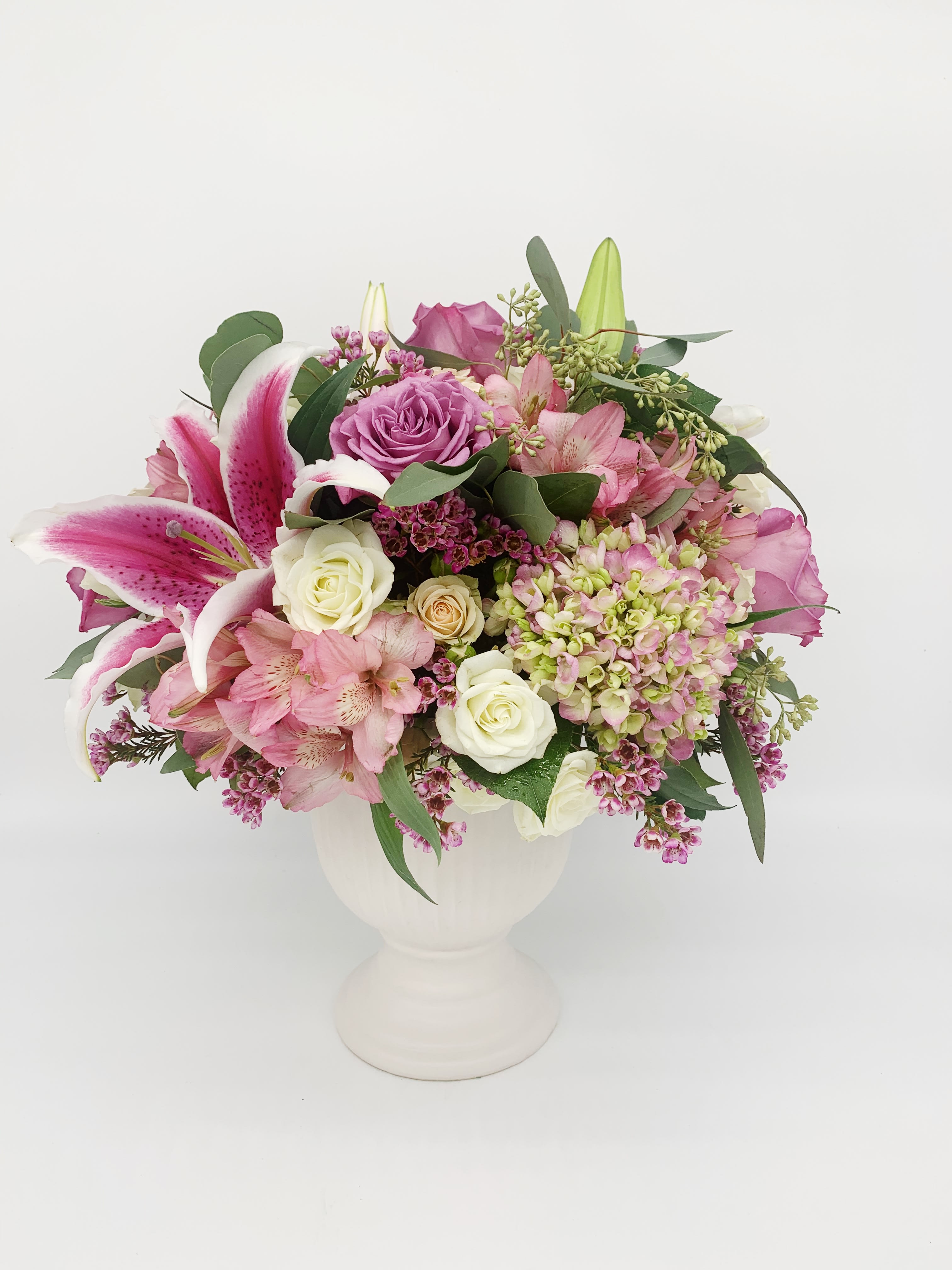 Pink and white mixed flower arrangement with lilies and roses in a white urn-style vase