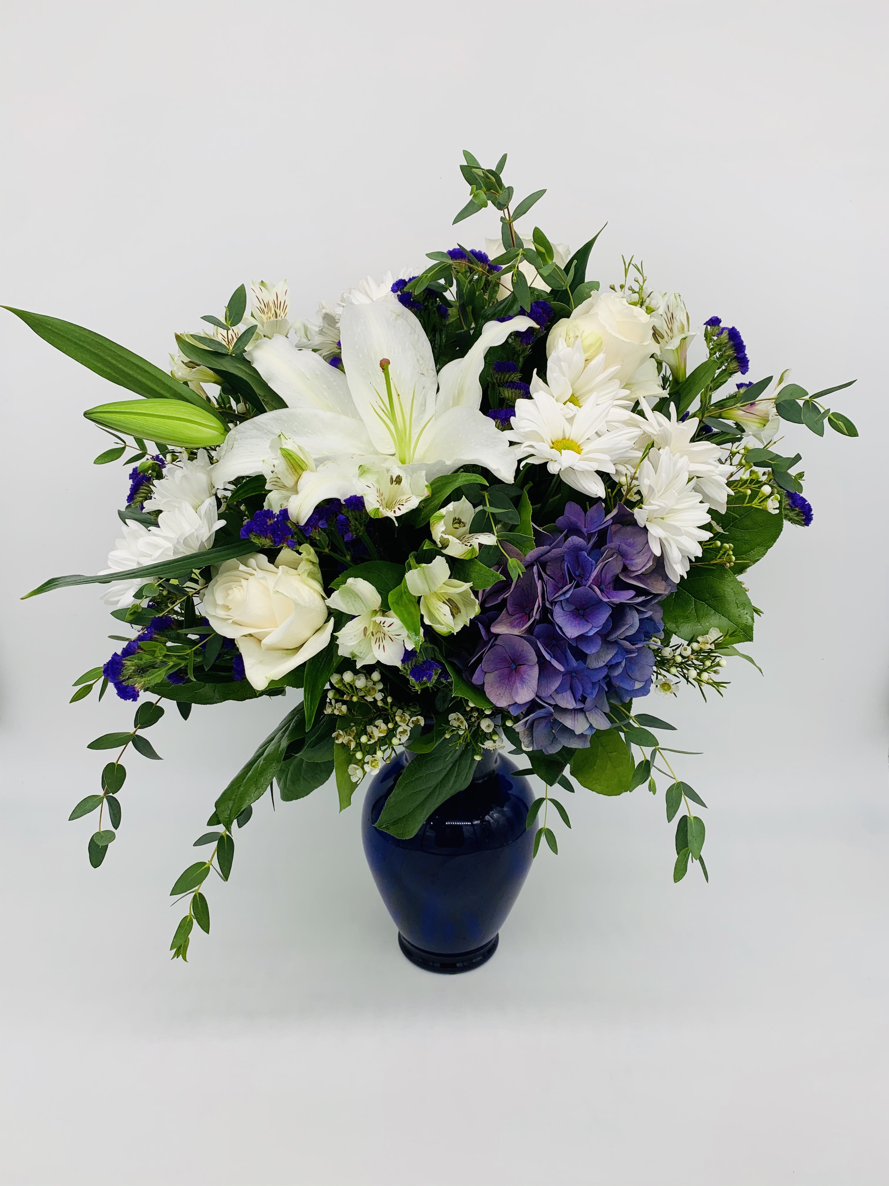 White and purple mixed flower arrangement in a navy blue vase