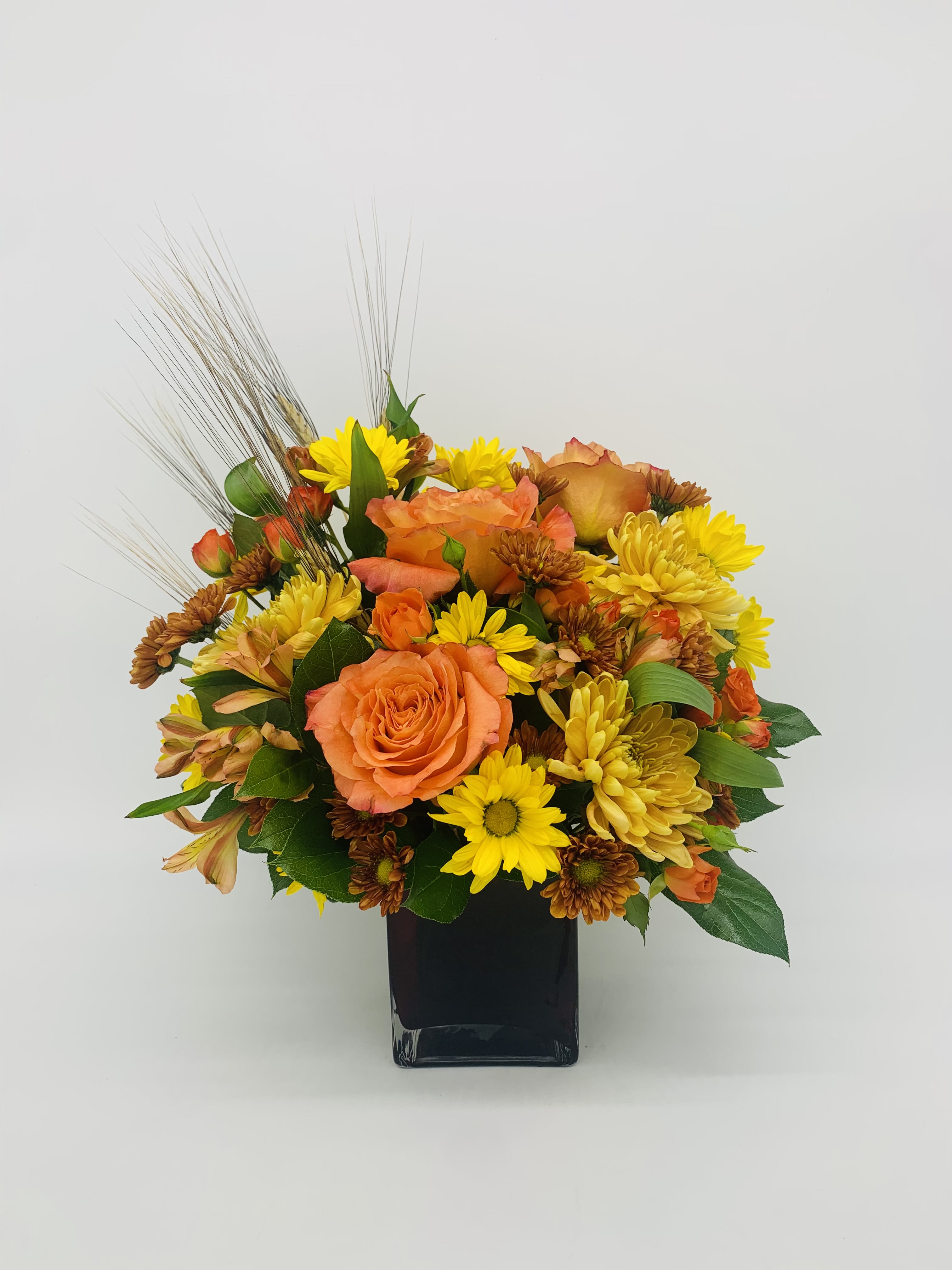 Compact arrangement of orange roses and yellow daisies in a black square vase