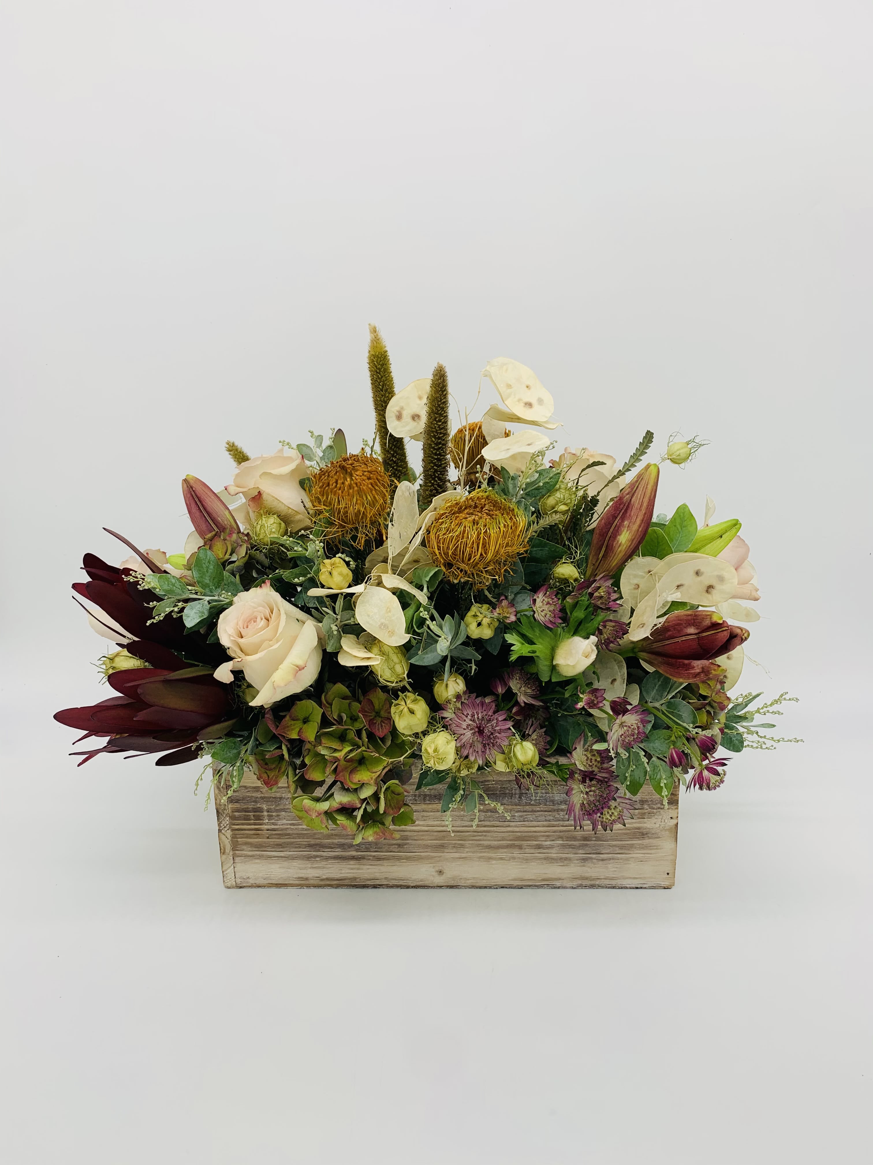 Low centerpiece of cream roses, golden protea, and mixed blooms in a rustic wooden box