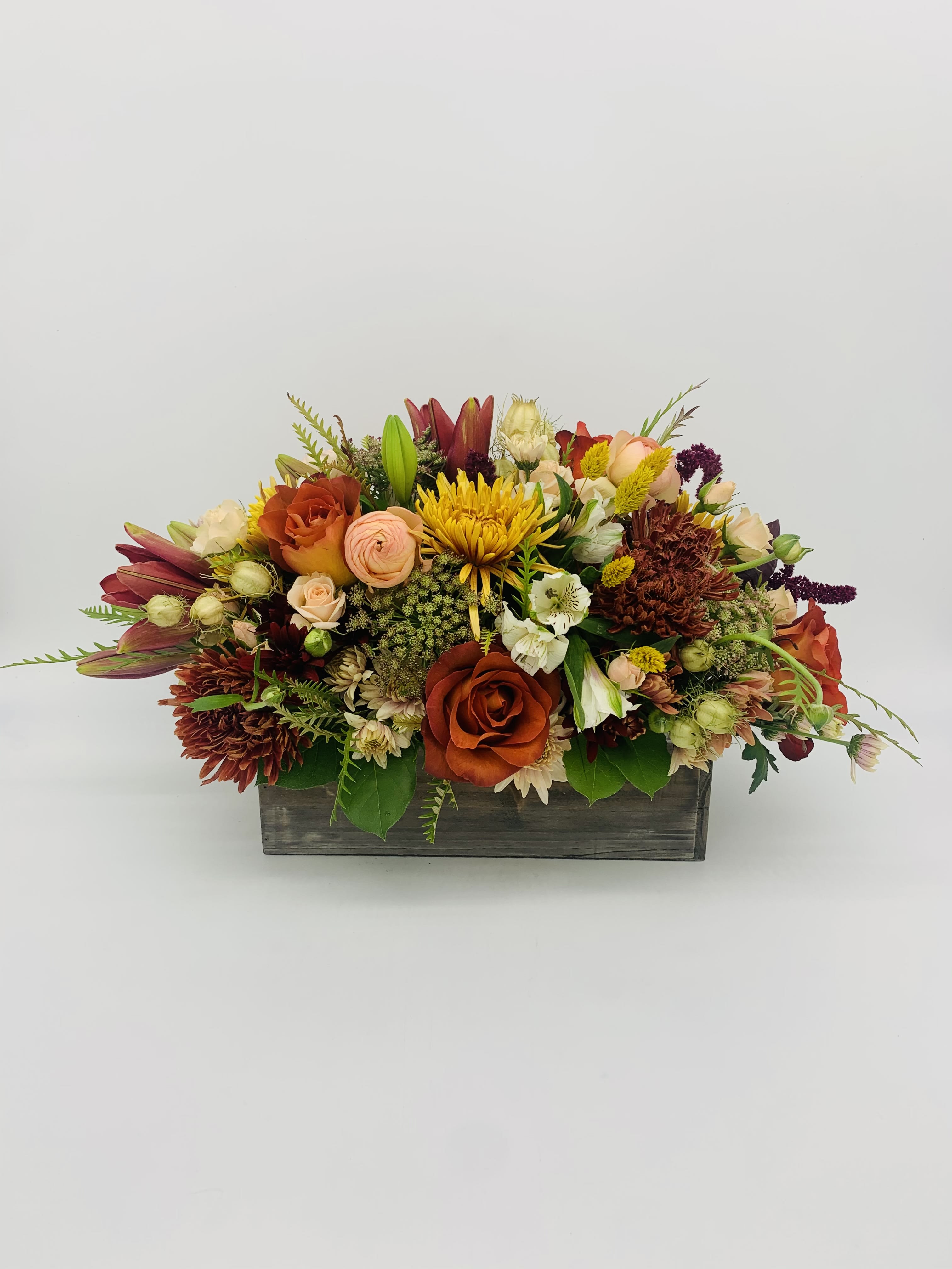 Low centerpiece of orange roses, yellow mums, and mixed flowers in a rustic wooden box.