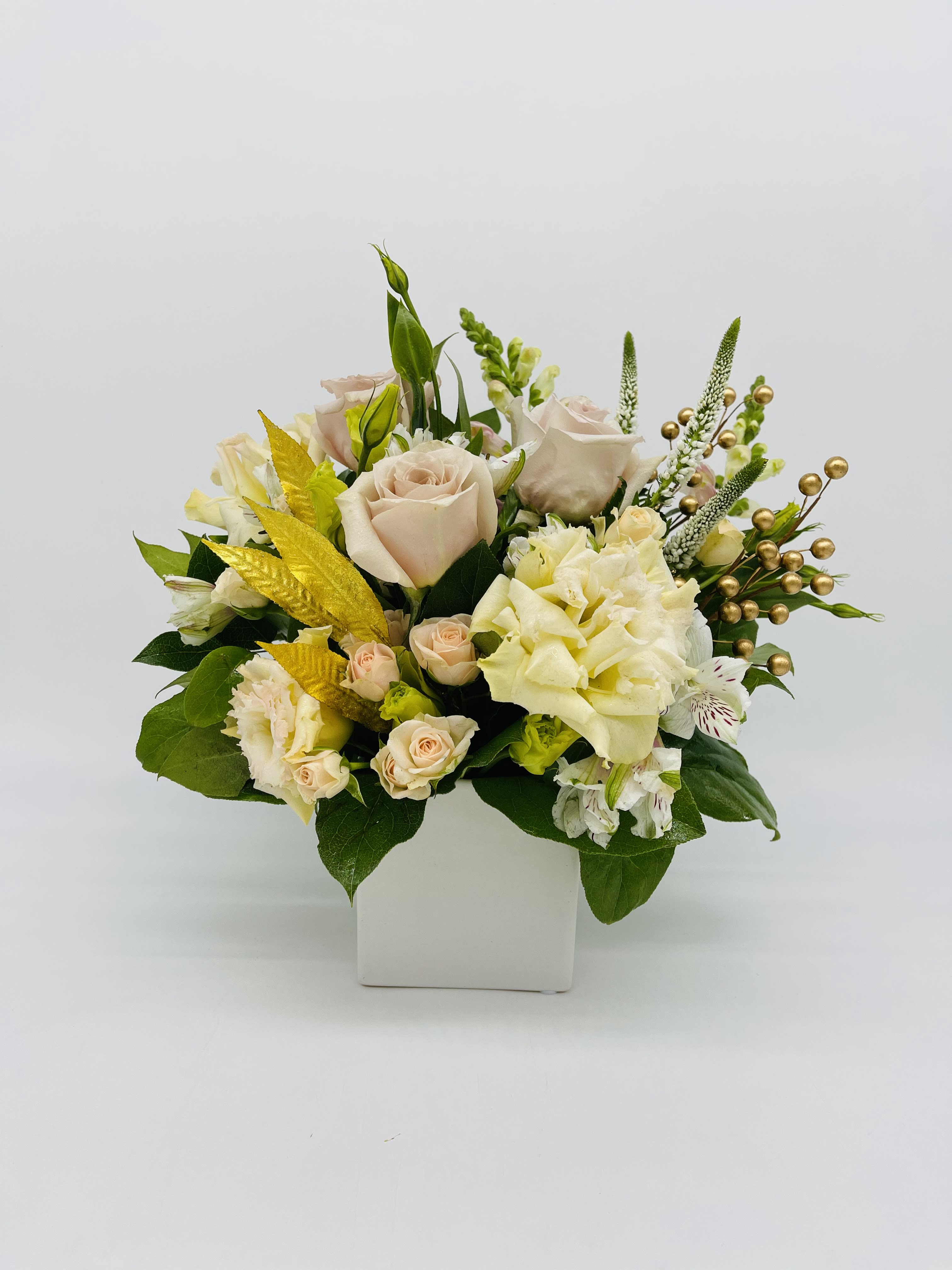 Low arrangement of cream roses and mixed white flowers in a square white vase