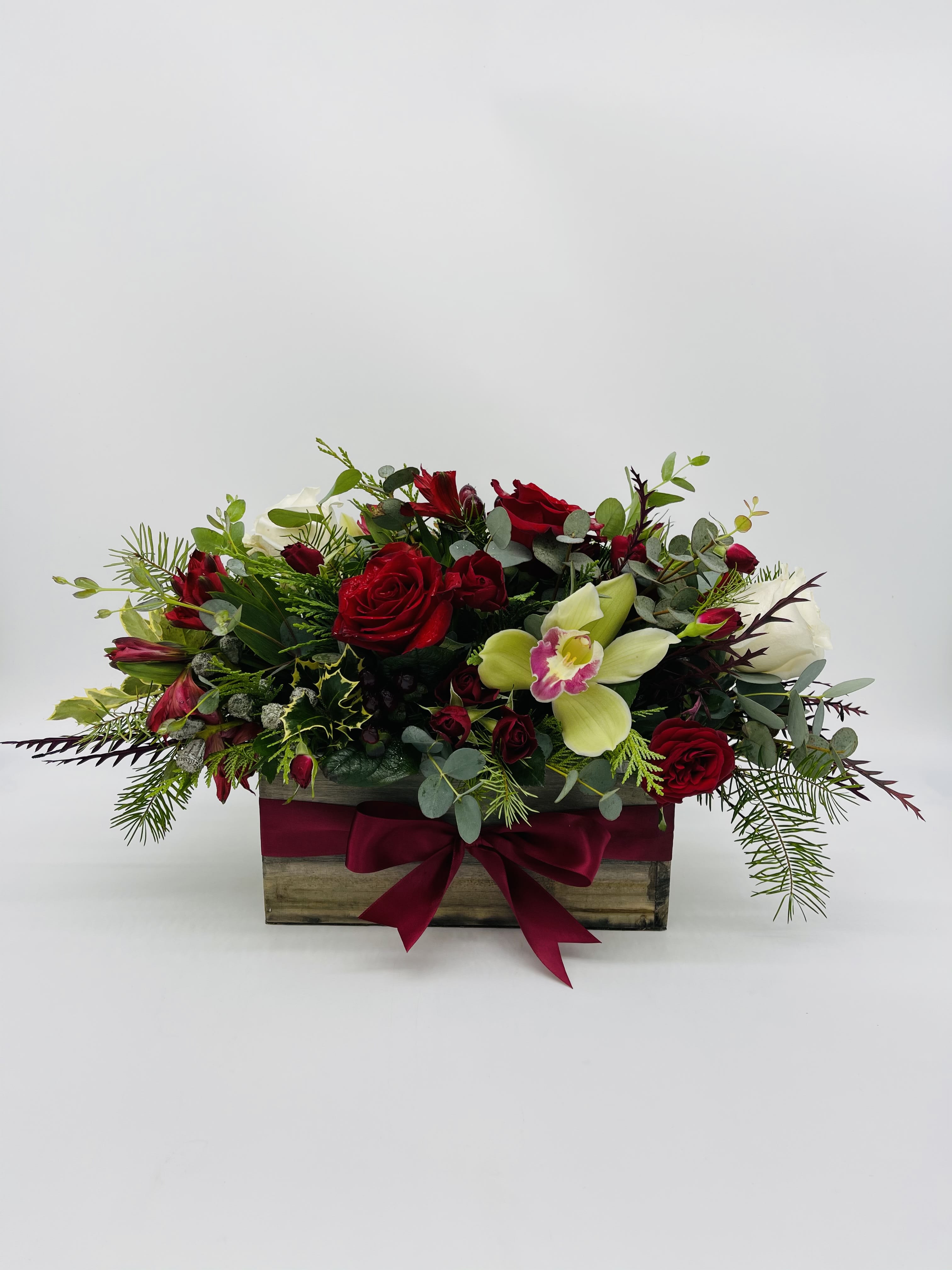 Low rectangular arrangement of red roses, white blooms, and green orchids in a wooden box with a red bow