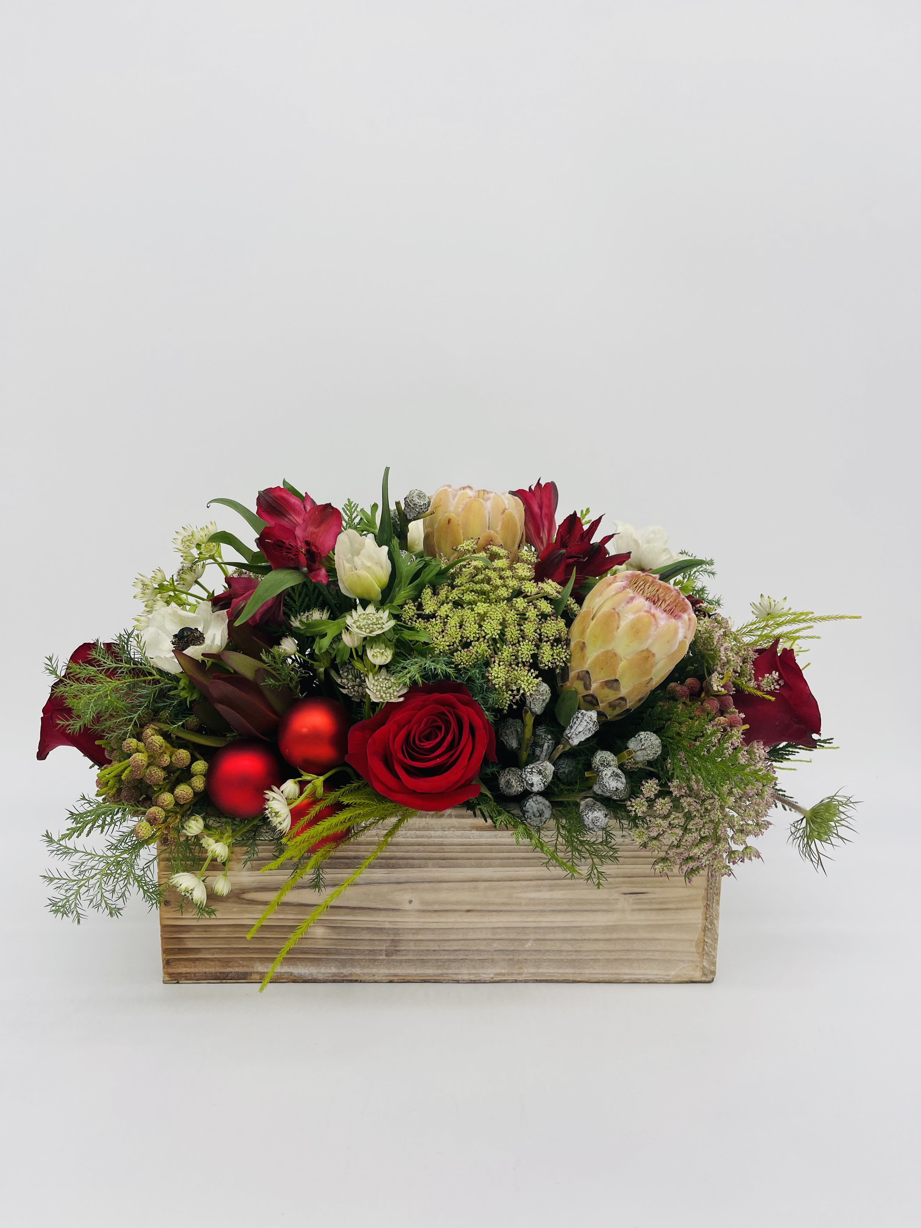 Low red and white flower arrangement with protea and roses in a wooden rectangular box with red ornaments.