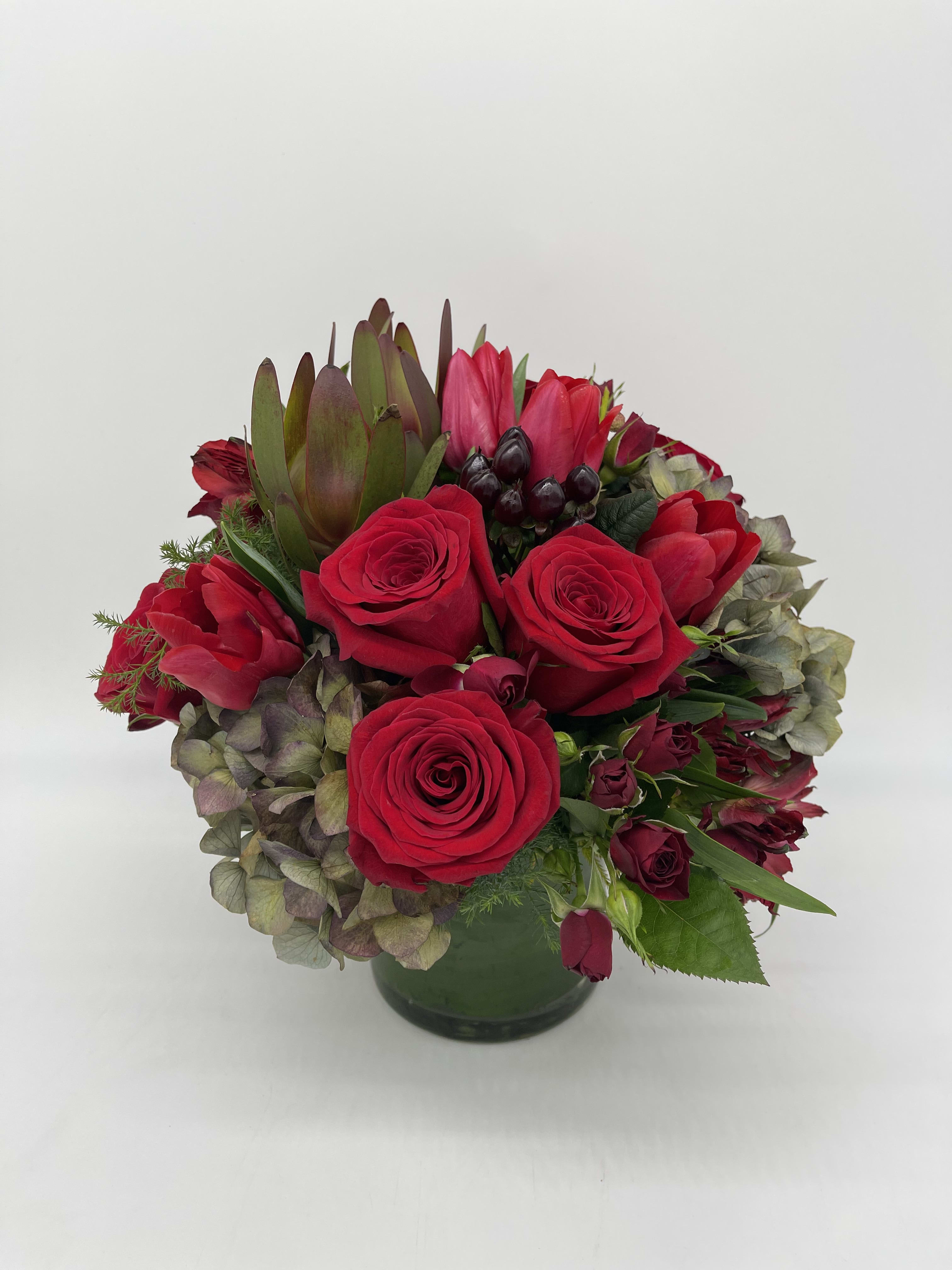 Low round arrangement of red roses with mixed hydrangeas in a glass vase