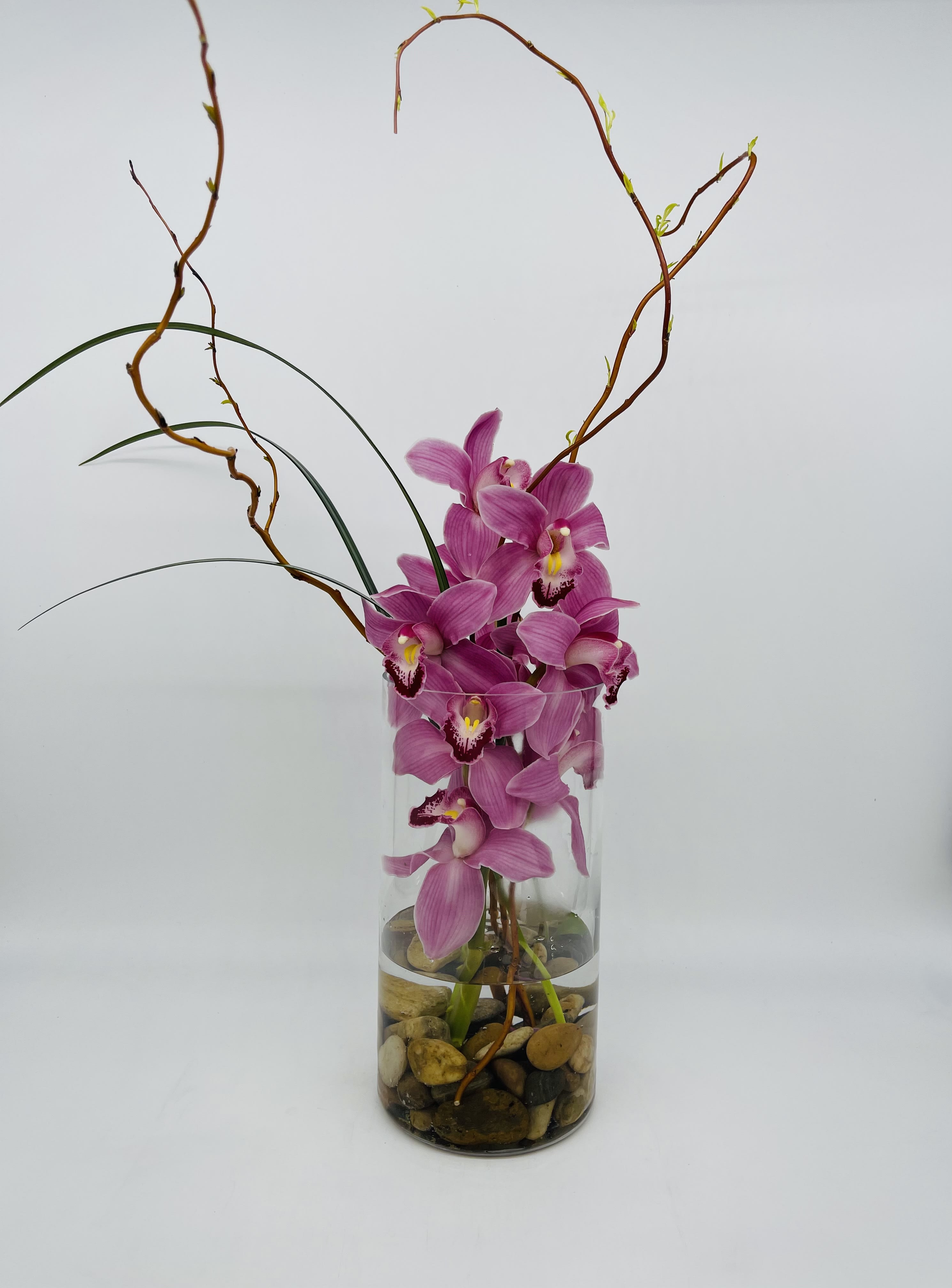 Tall pink orchid arrangement in a clear glass cylinder vase with river stones at the base