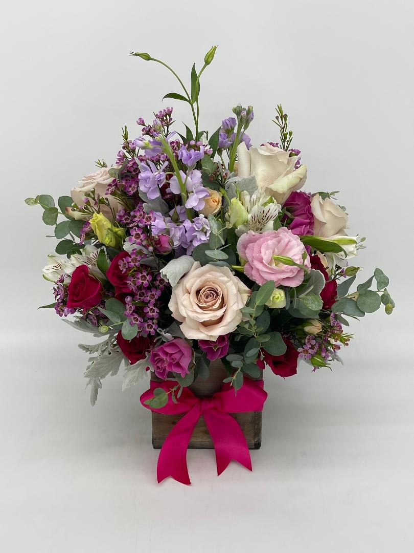 Mixed pink, red, and cream flower arrangement in a wooden cube with a bright pink bow.