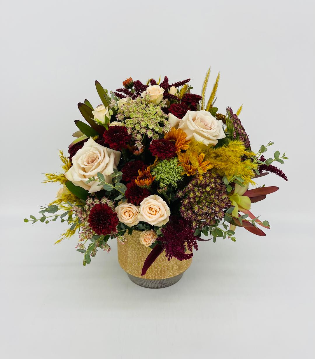Low arrangement of cream roses and burgundy mums with golden accents in a gold ceramic vase