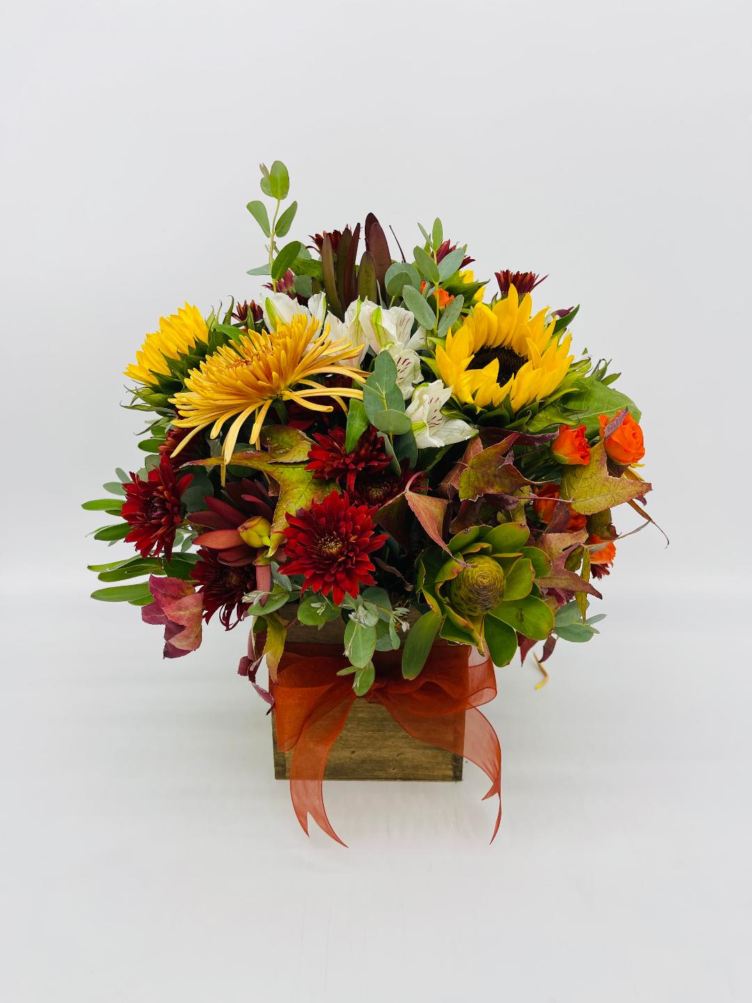 Square wooden vase arrangement with yellow sunflowers, red mums, white blooms, and orange accents.