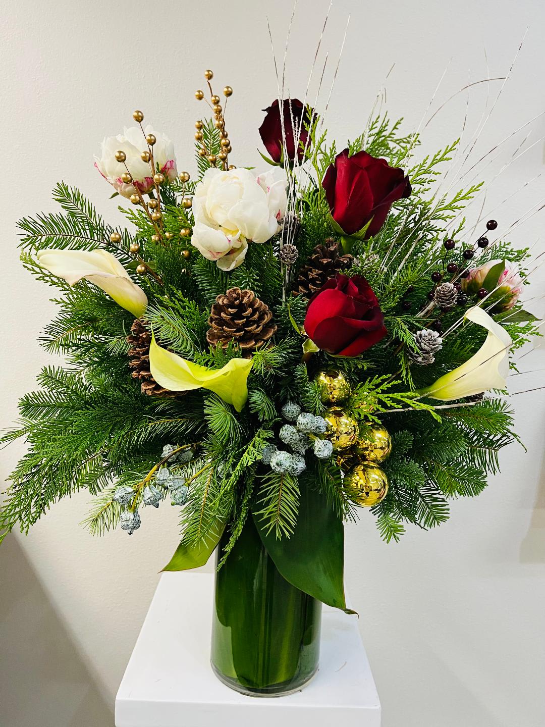 Tall holiday arrangement with red roses, white blooms, calla lilies, evergreens, pinecones and gold ornaments in a green vase