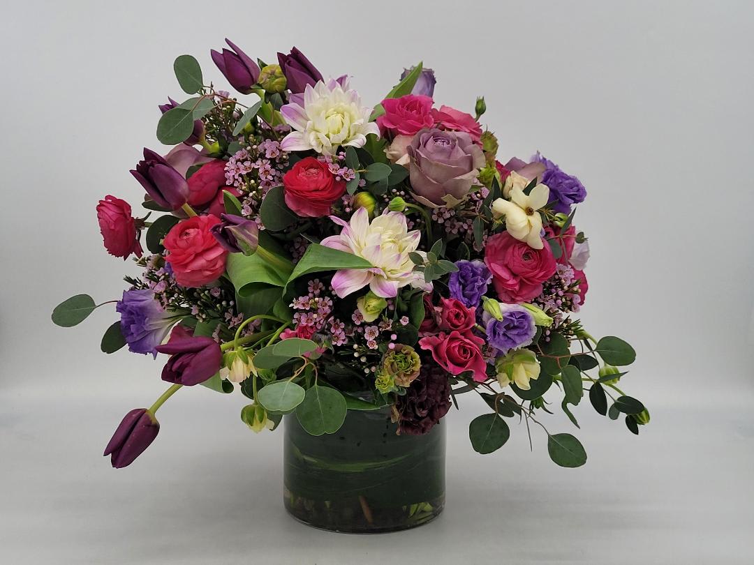 Lush arrangement of pink, purple and white mixed flowers in a clear glass vase