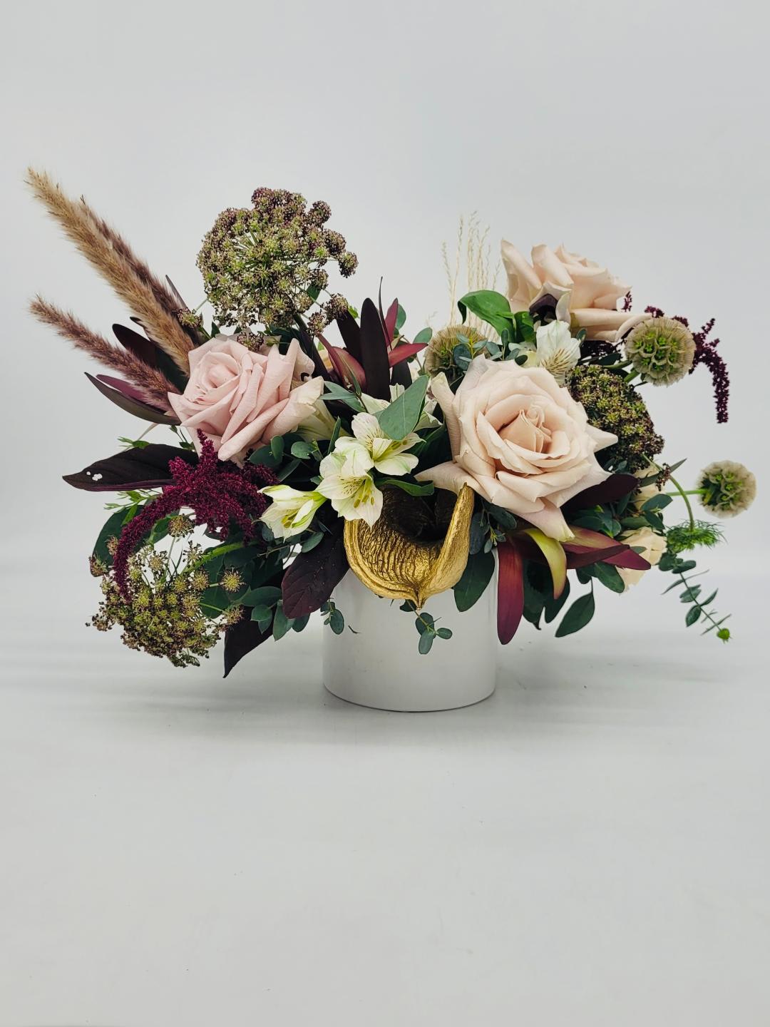 Low arrangement of blush roses, white blooms and textured accents in a white cylinder vase