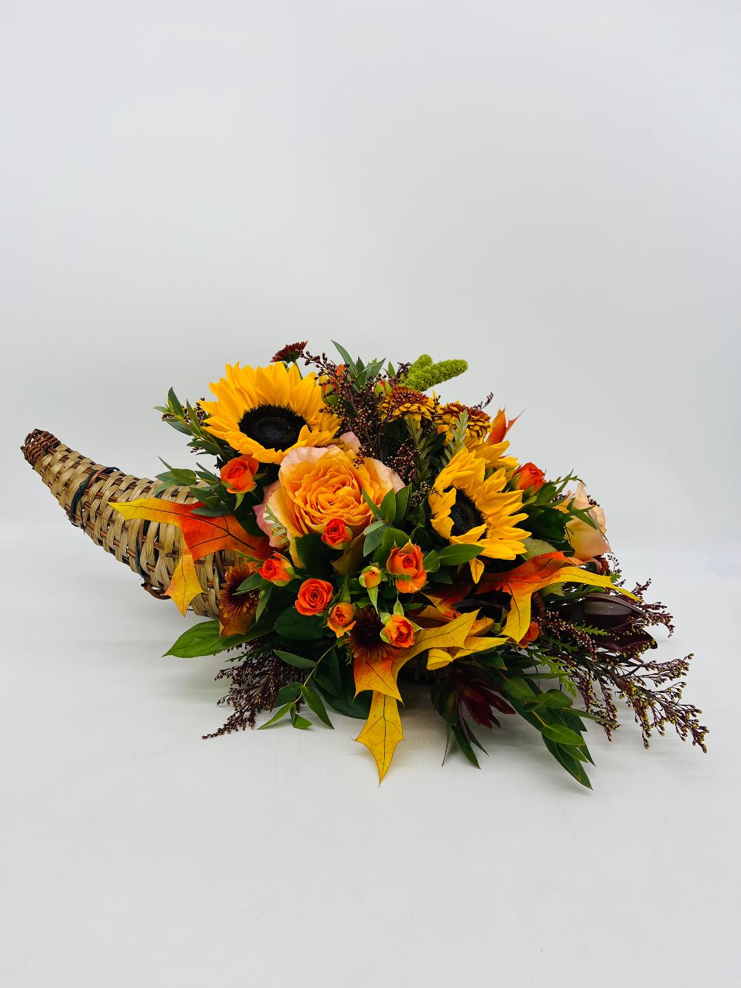 Autumn cornucopia with yellow sunflowers and orange roses in a woven horn basket