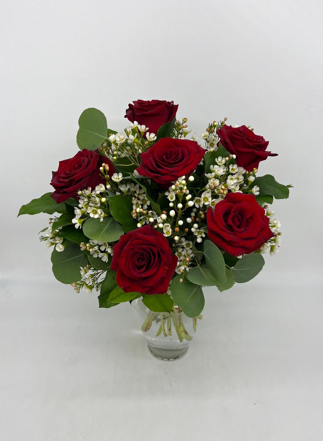 Small arrangement of red roses with tiny white filler blooms in a clear glass vase