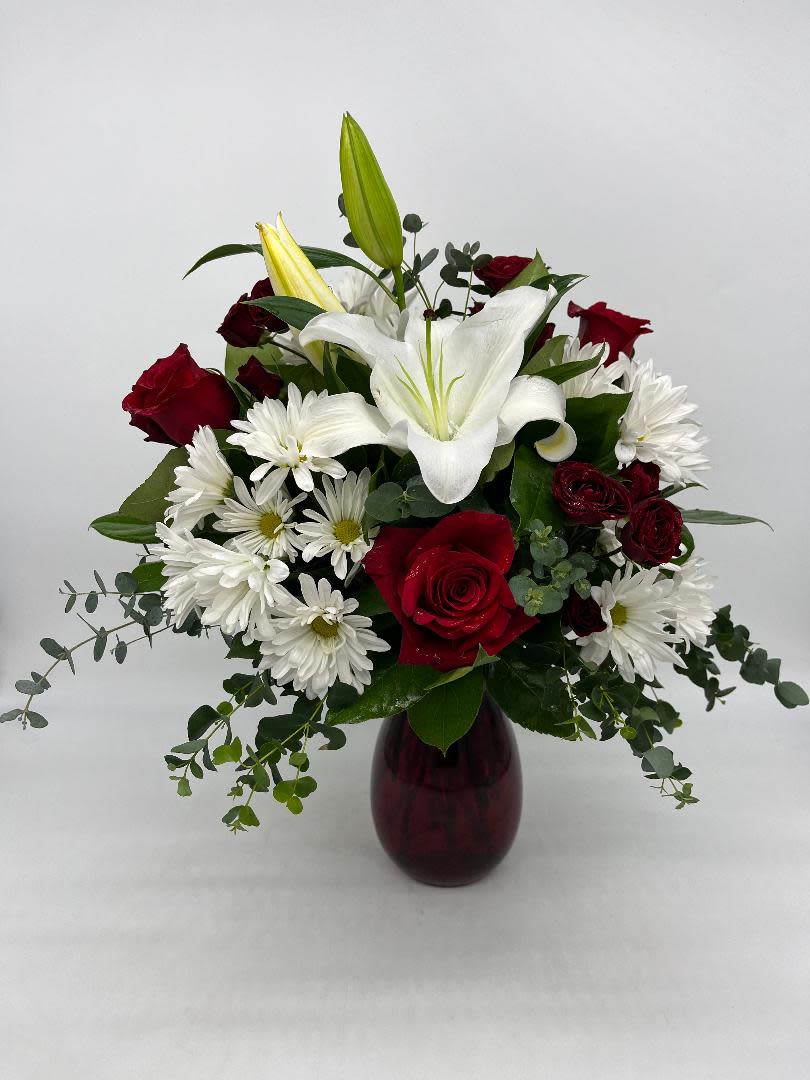 Red roses, white lilies, and white daisy mums arranged in a red glass vase