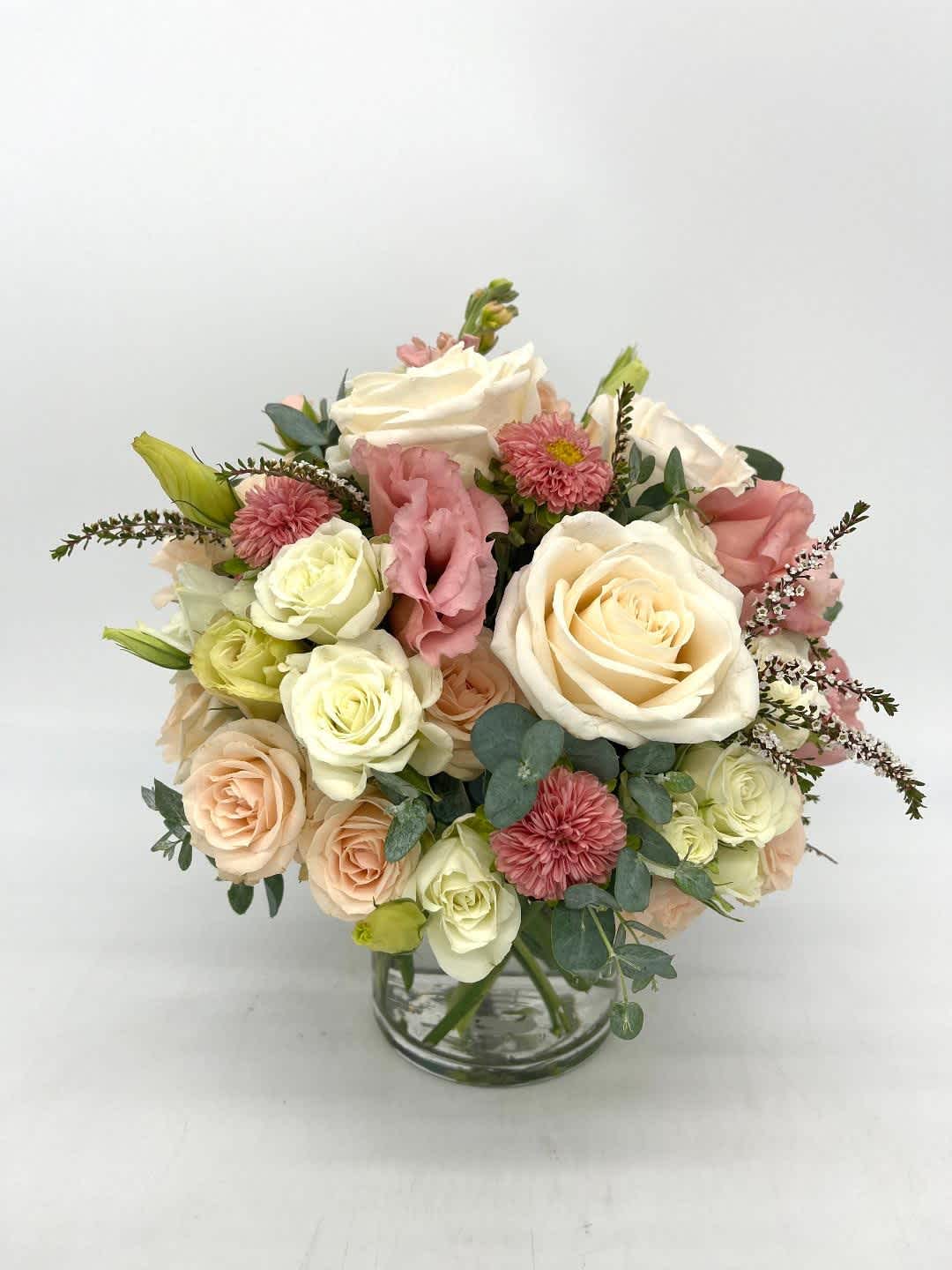 Round arrangement of white and peach roses with pink blooms in a clear glass vase