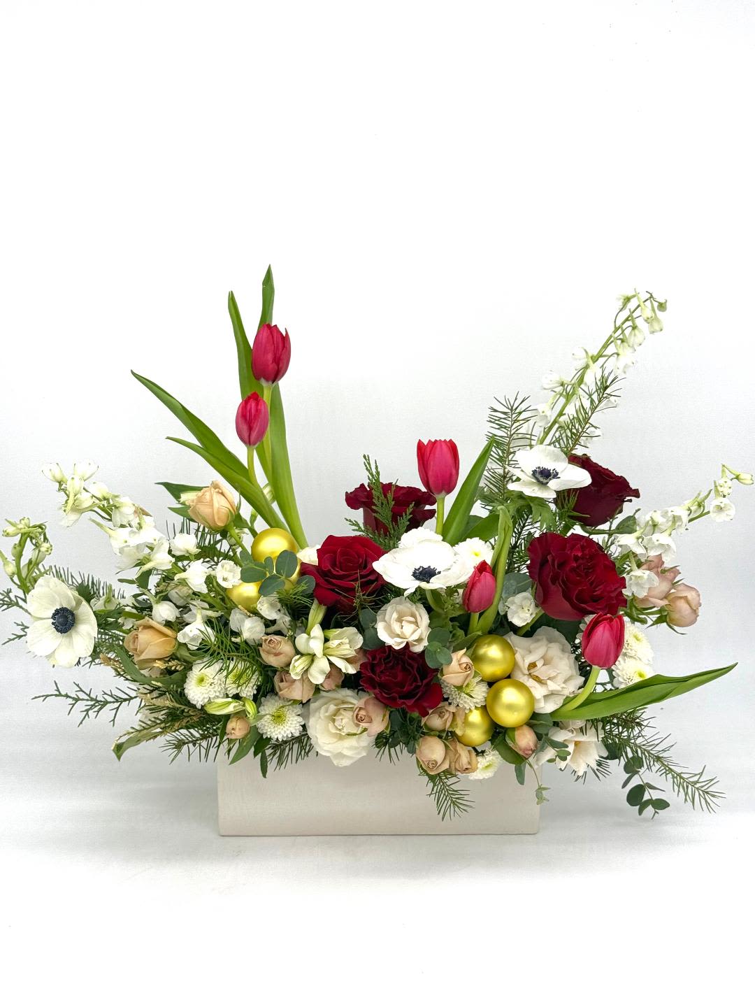 Low red and white floral arrangement with tulips, roses, anemones and gold ornaments in a white rectangular container